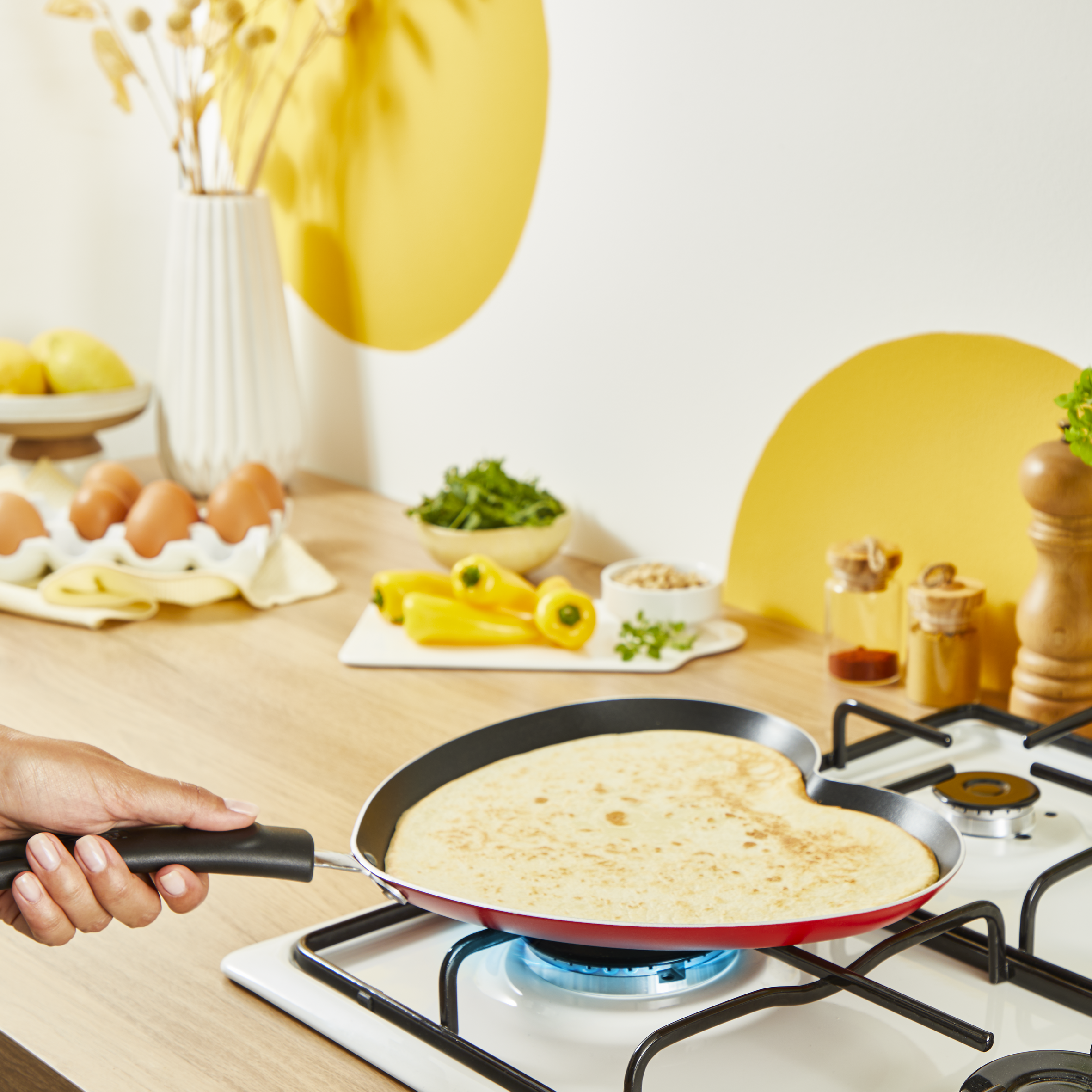 Naleśnik na patelni w kształcie serca na kuchence. Jajka, papryka i inne składniki w pobliżu.