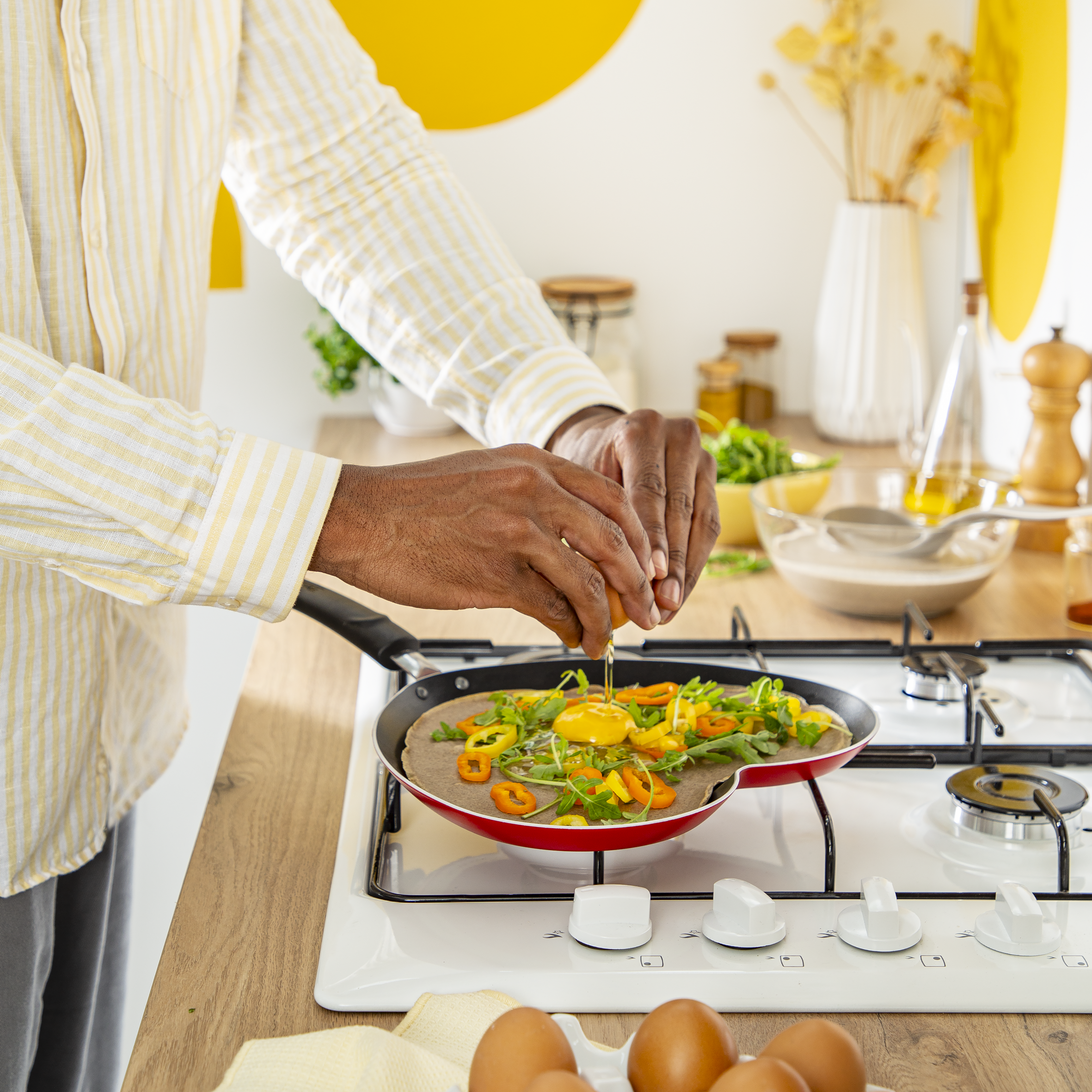 Osoba wbija jajko do patelni z warzywami. Gotowanie na kuchence w jasnej kuchni.
