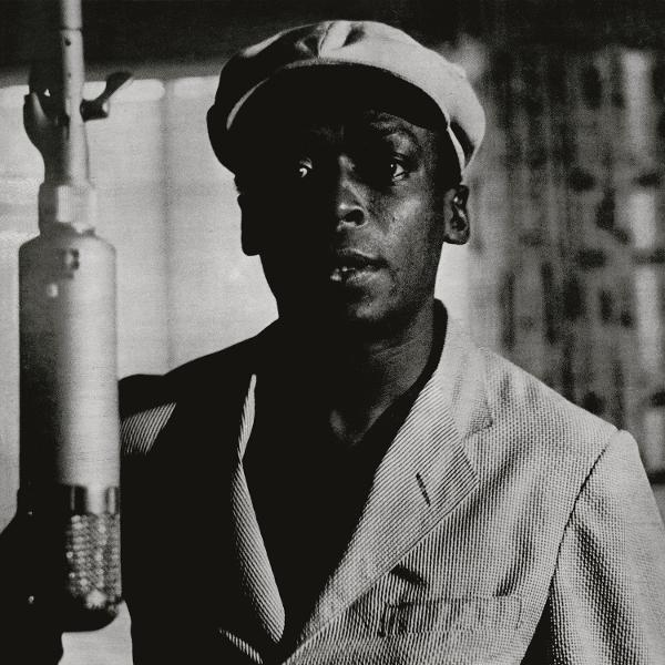 Miles Davis fekete-fehér fotója, öltönyben, mikrofonnal.