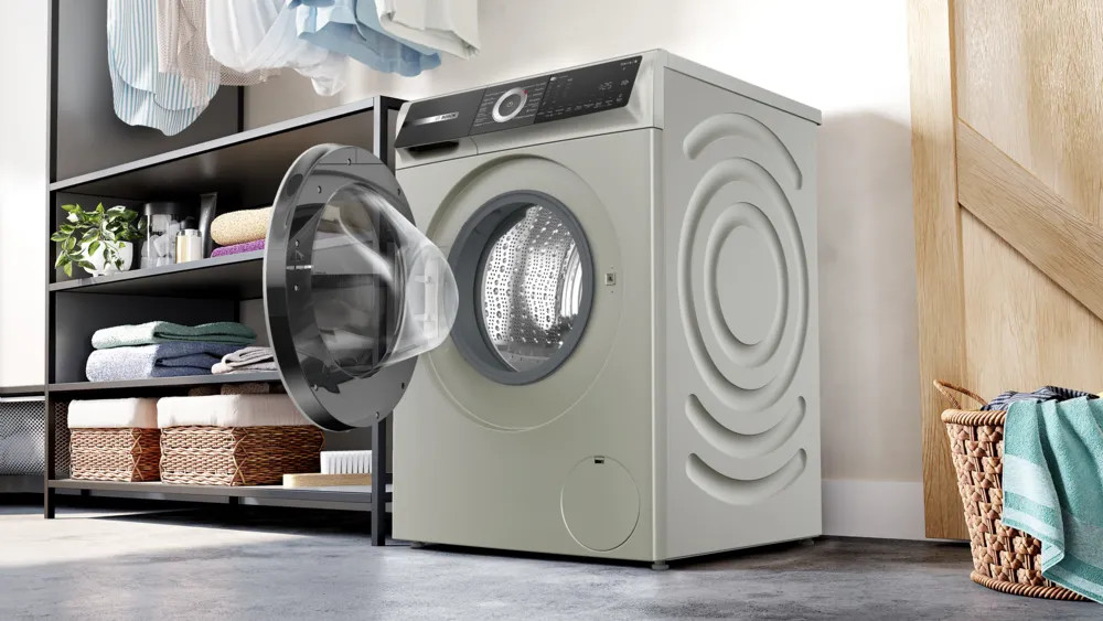 Pralka z otwartymi drzwiami, pralnia. Na tle półka ze złożonymi ręcznikami.