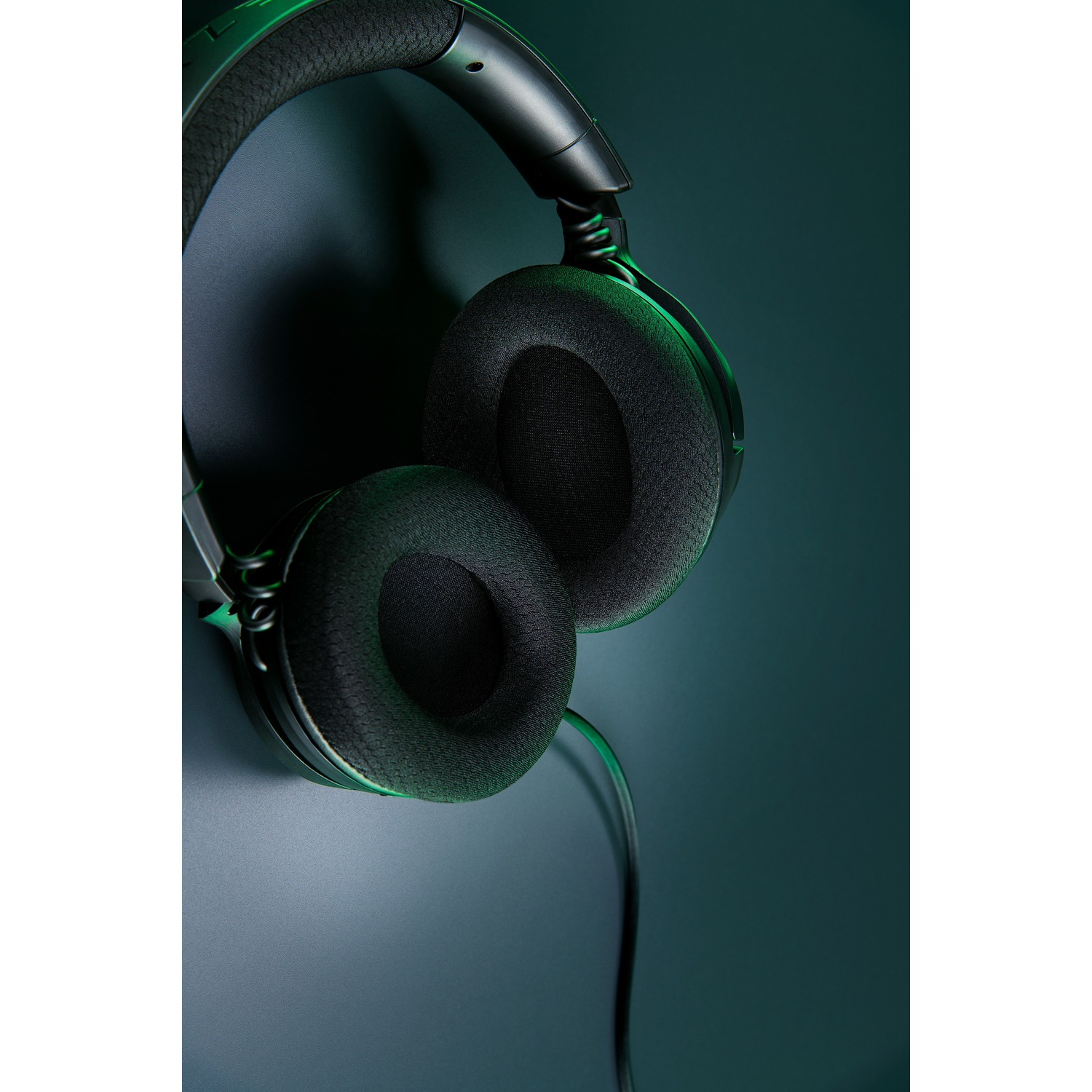 Black headphones on a dark blue background, with a green light illuminating them.