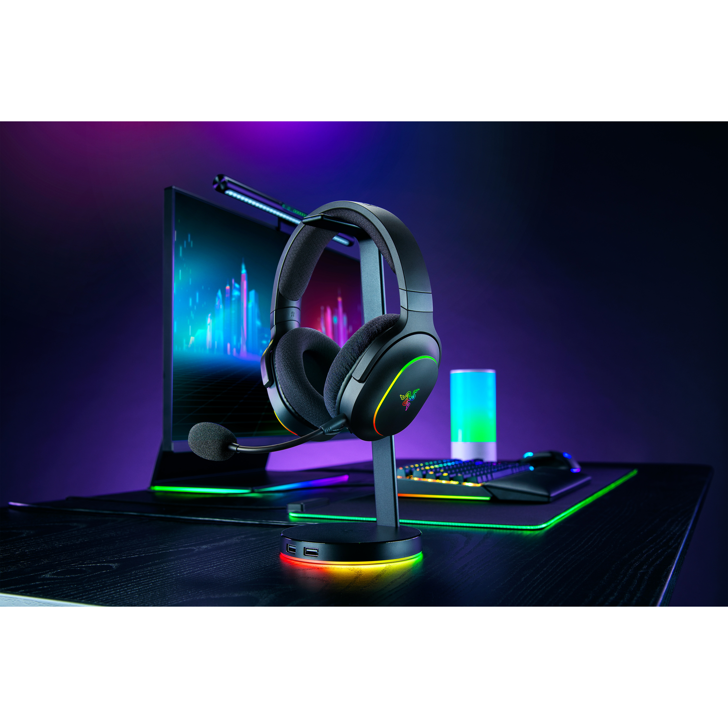A black headset on a stand, with a monitor behind. The monitor has colorful light.