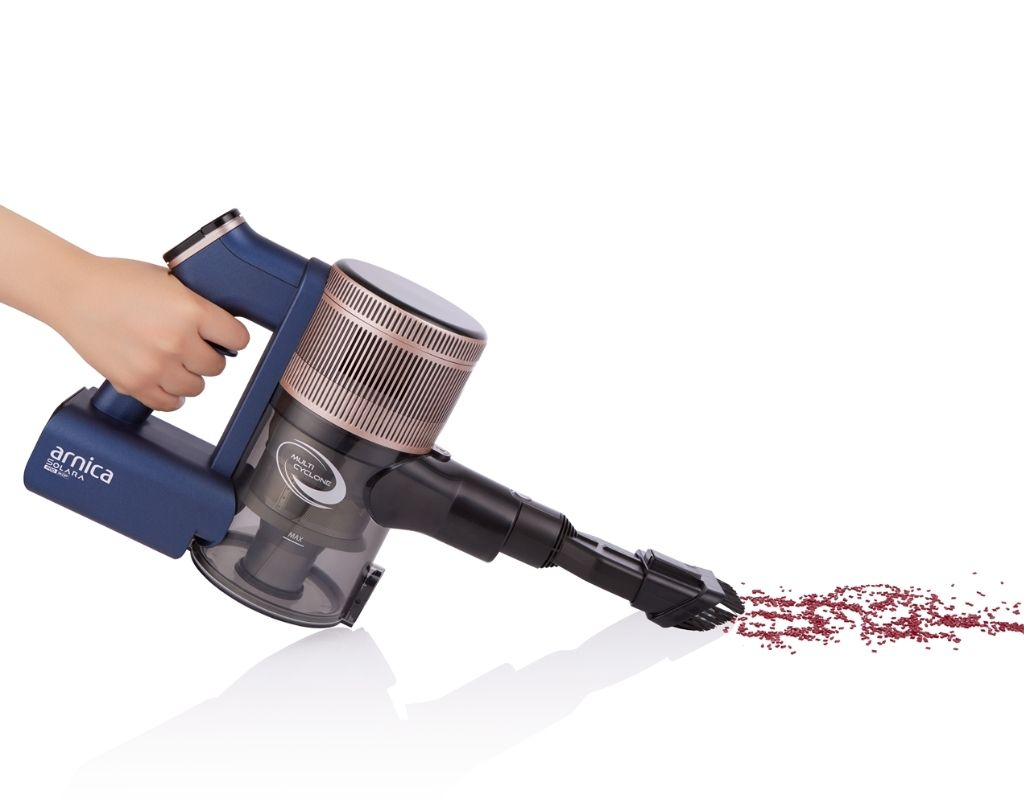 Mavi ve altın rengi bir elektrikli süpürge tutan bir el ve elektrikli süpürge dökülen kırmızı boncukları süpürüyor.