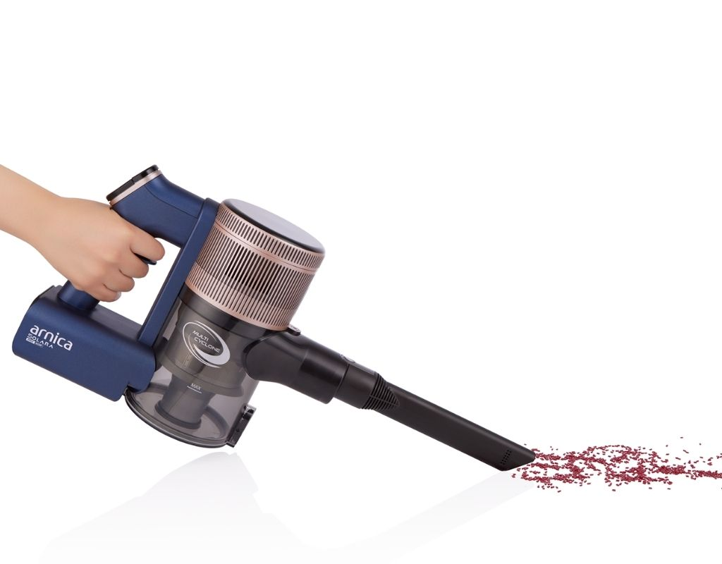 Bir el, kırmızı bir enkaz izi üzerinde mavi ve altın renkli bir elektrikli süpürge tutuyor.