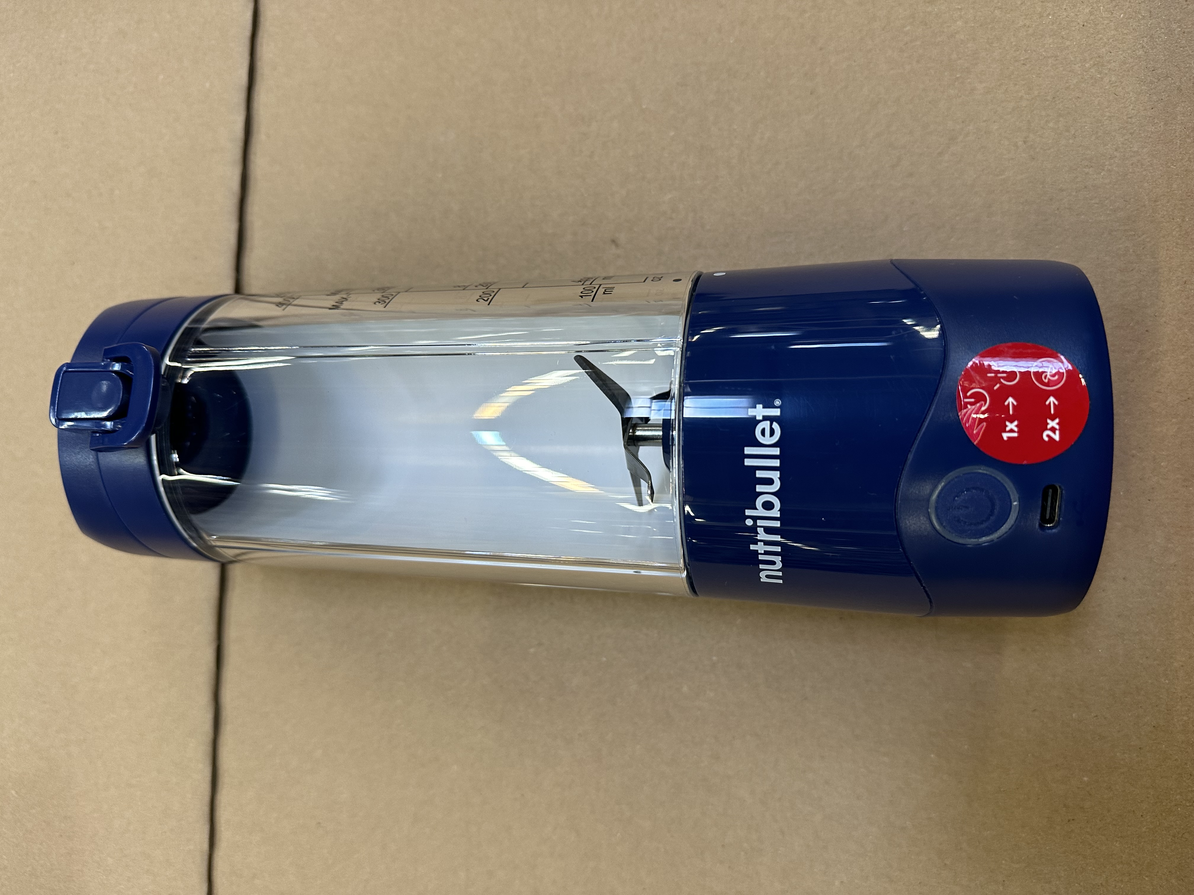 Niebieski i przezroczysty blender Nutribullet. Ma ostrze, przycisk zasilania i ustawienia prędkości.