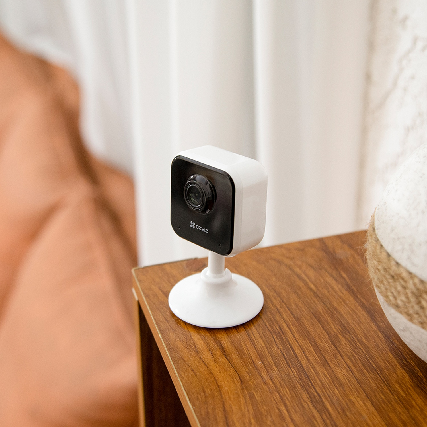 Una piccola telecamera di sicurezza bianca su un tavolo di legno, con sfondo bianco.