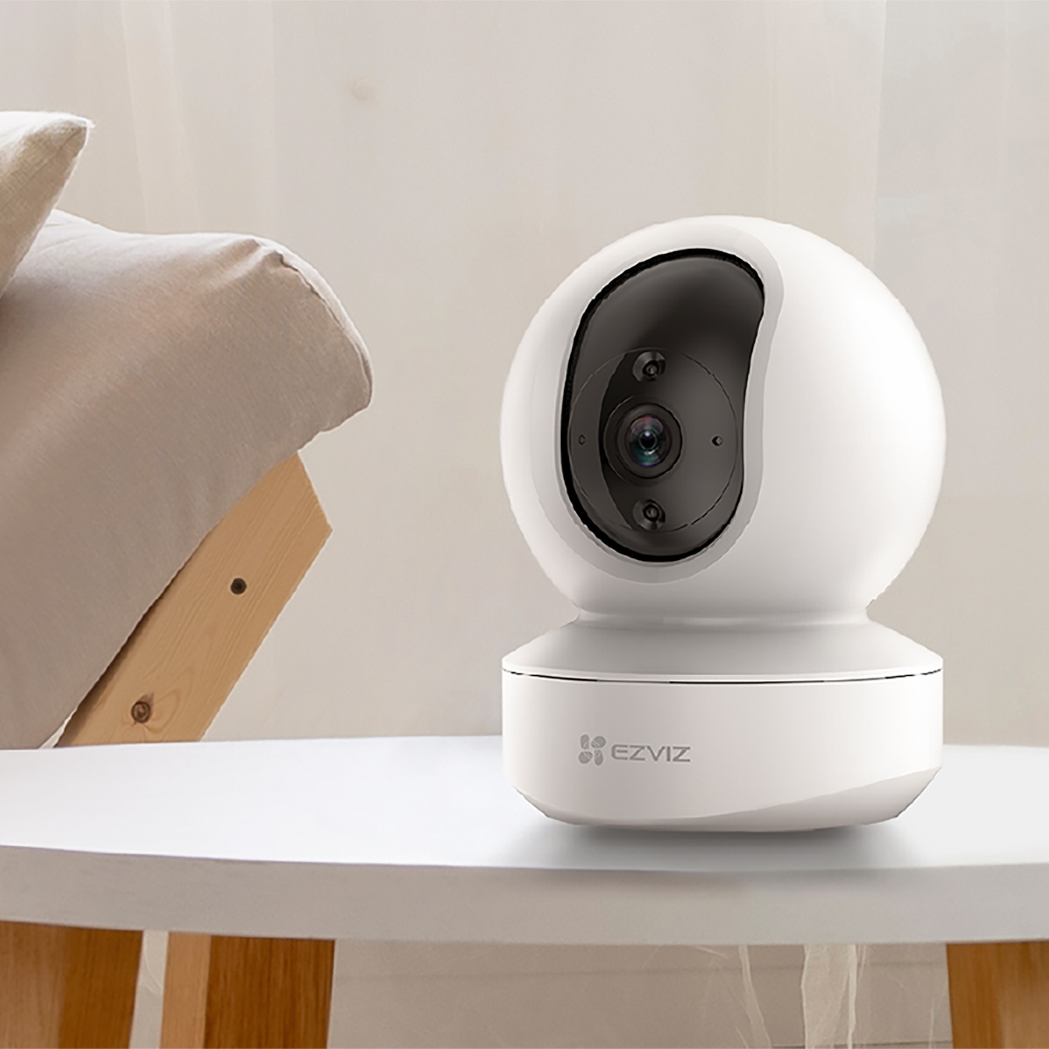 Telecamera di sicurezza domestica intelligente bianca su un tavolo. Lo sfondo mostra una stanza illuminata.