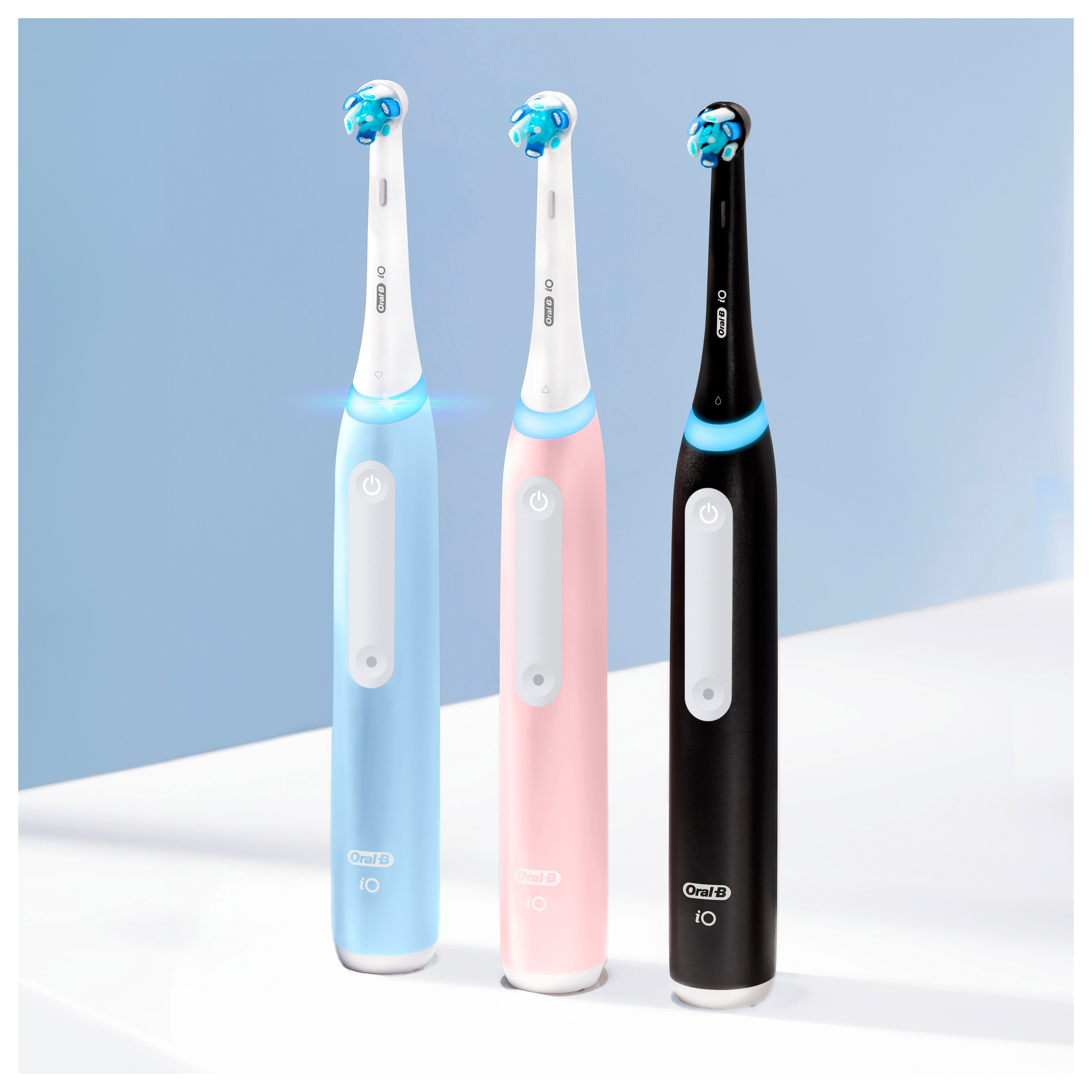 Trois brosses à dents électriques, bleues, roses et noires, sur une surface claire.