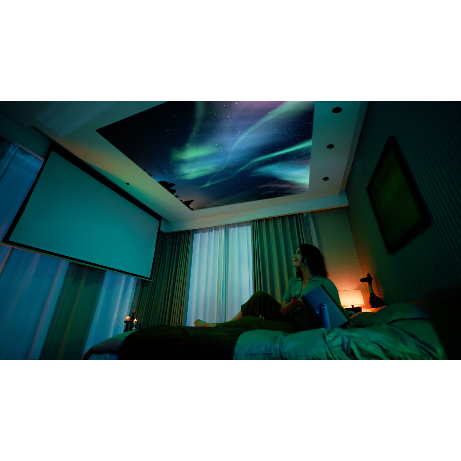 Een vrouw zit op een bed en bekijkt een tablet. Een afbeelding van het noorderlicht wordt op het plafond geprojecteerd.