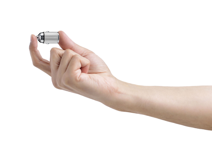 Eine Hand, die einen kleinen, metallischen, zylindrischen Gegenstand zwischen Daumen und Zeigefinger hält.