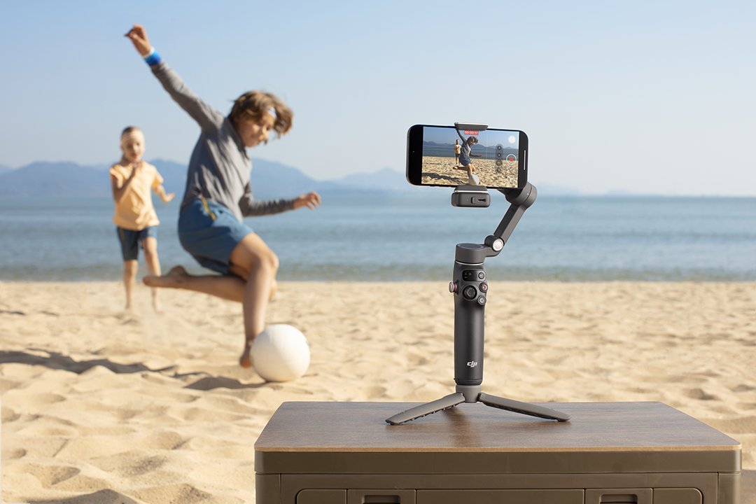 Egy fiú rögzíti a barátját, amint focizik a strandon egy fekete gimballel.