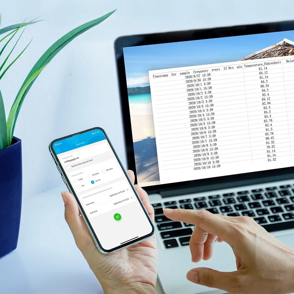 Osoba trzymająca telefon z wykresem i laptopem w tle, w pomieszczeniu.