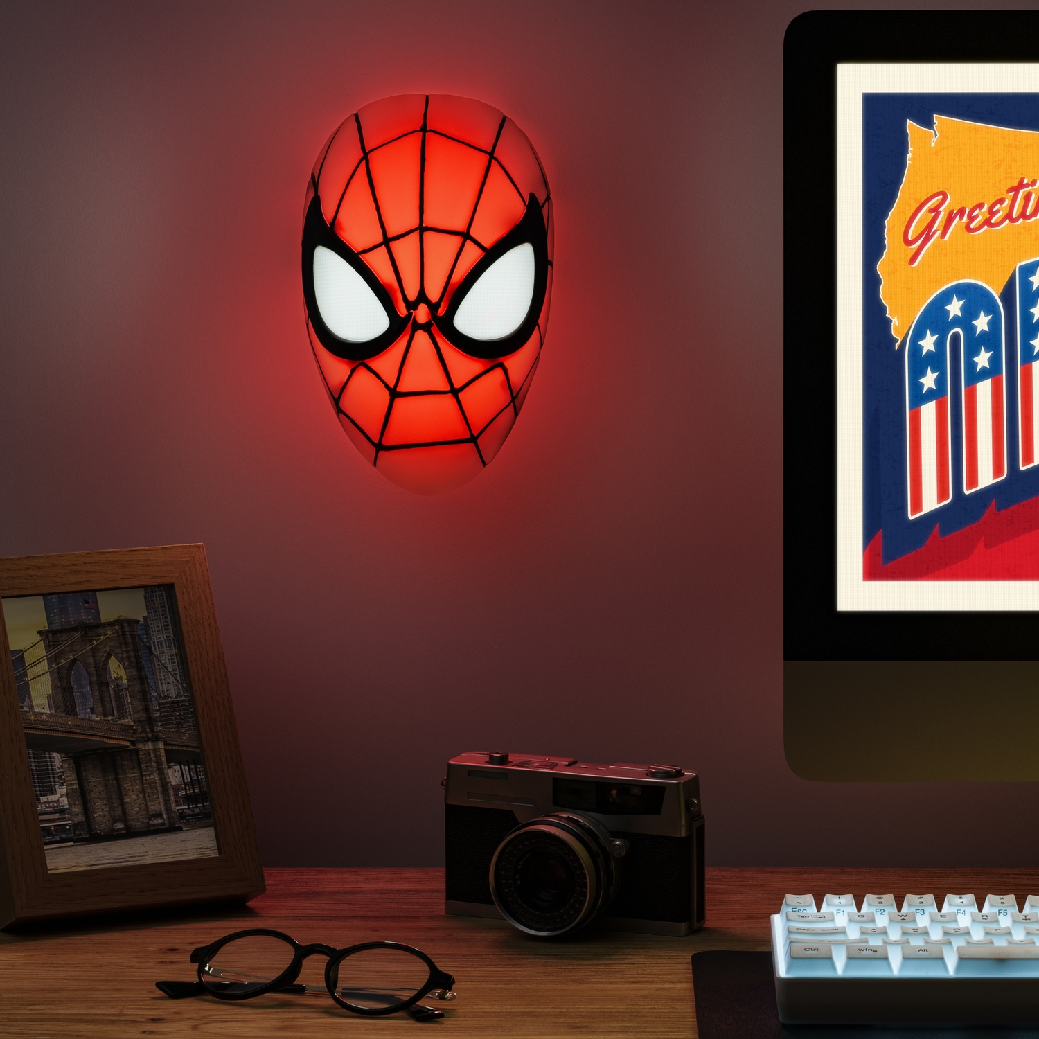 Een Spiderman-masker wandlamp met andere items op een bureau en een monitor.
