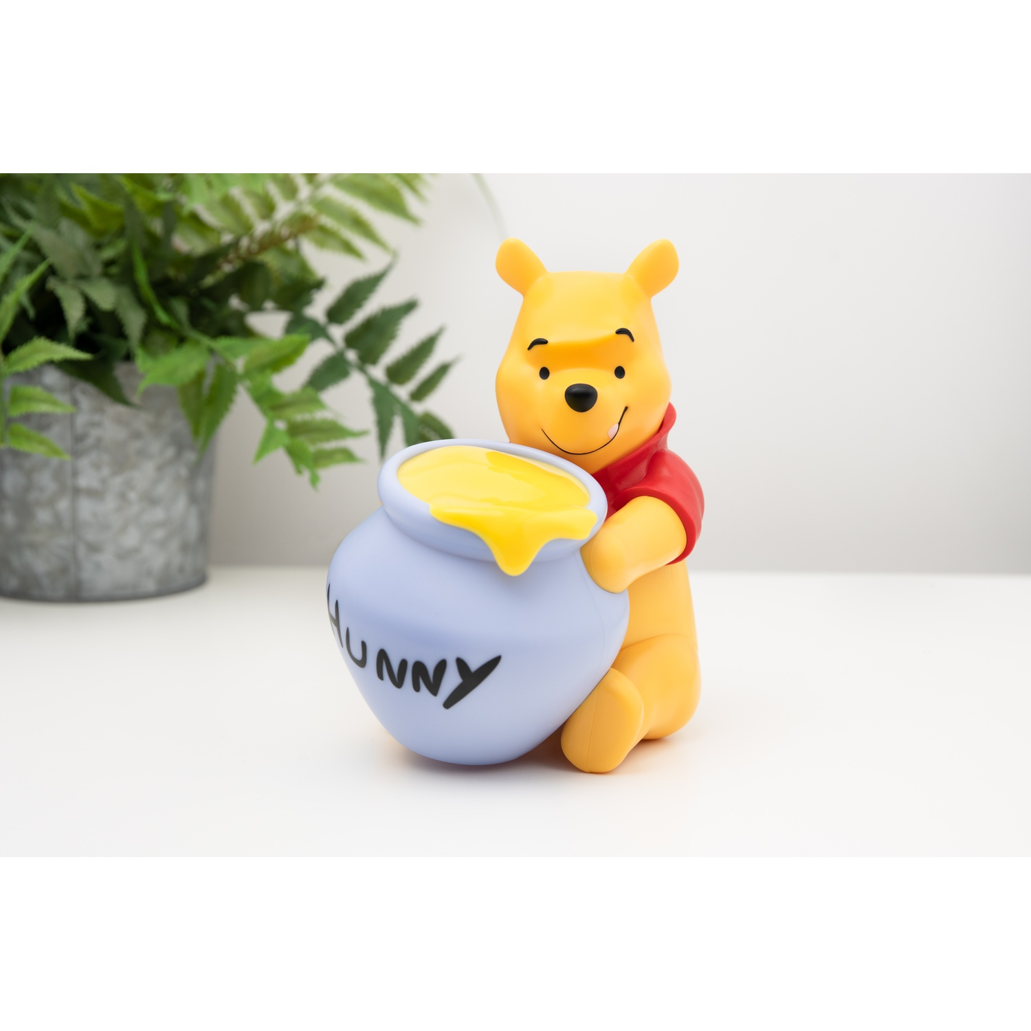 Winnie l'ourson tenant un pot de miel, sur une surface blanche.