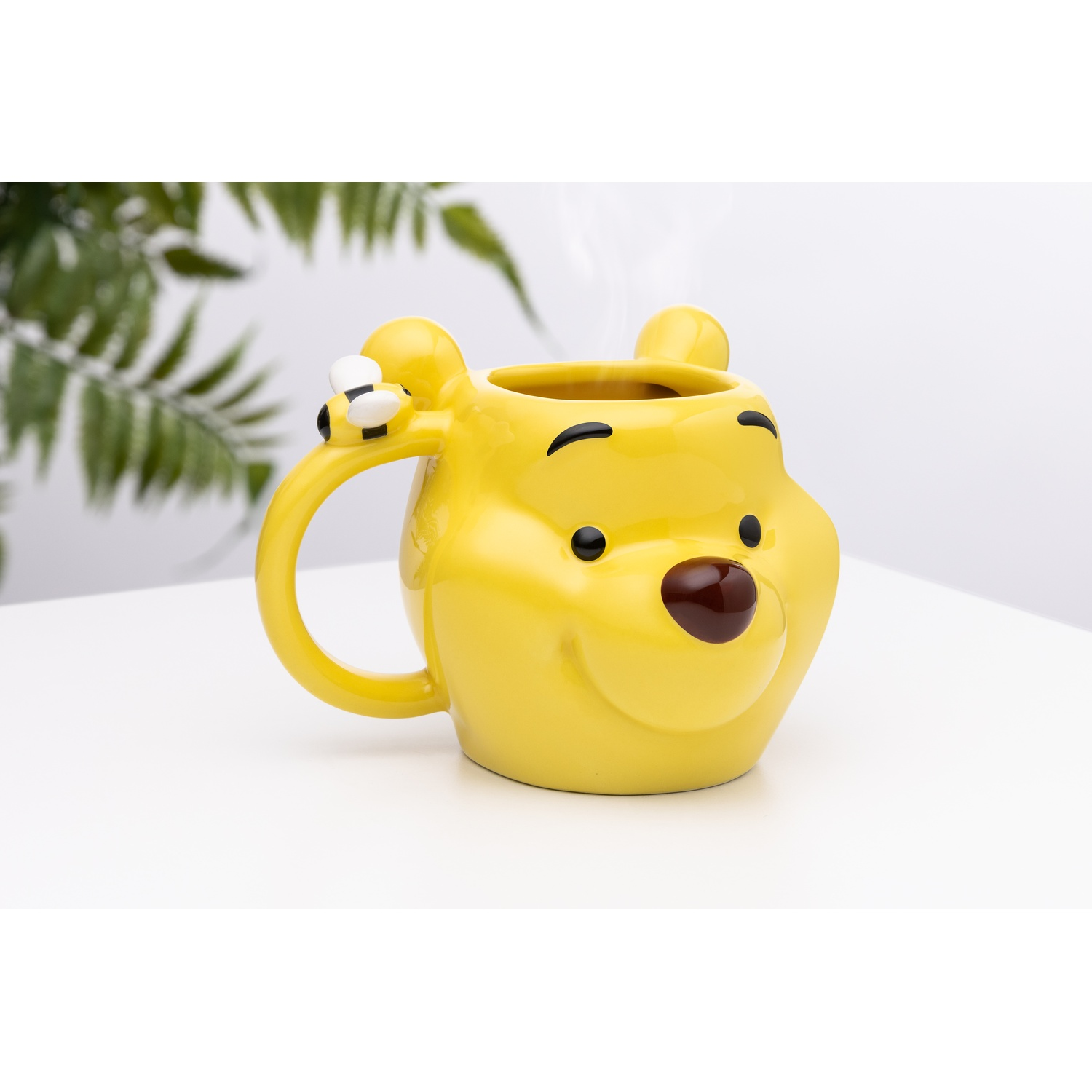 Yellow Winnie the Pooh mug with a bee, on white surface. Steam is rising from the top.