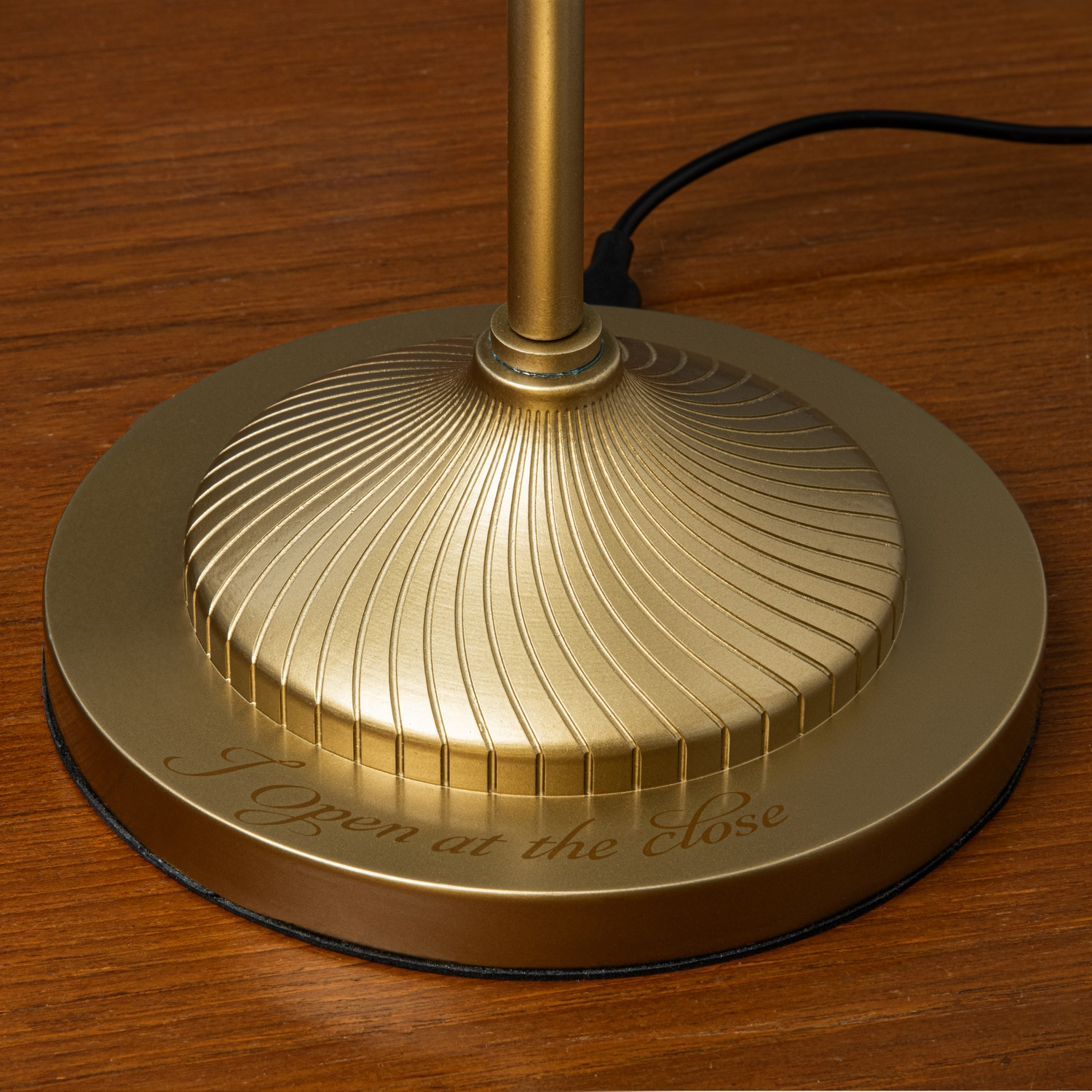 Gouden lampvoet met geëtste tekst, op houten oppervlak.