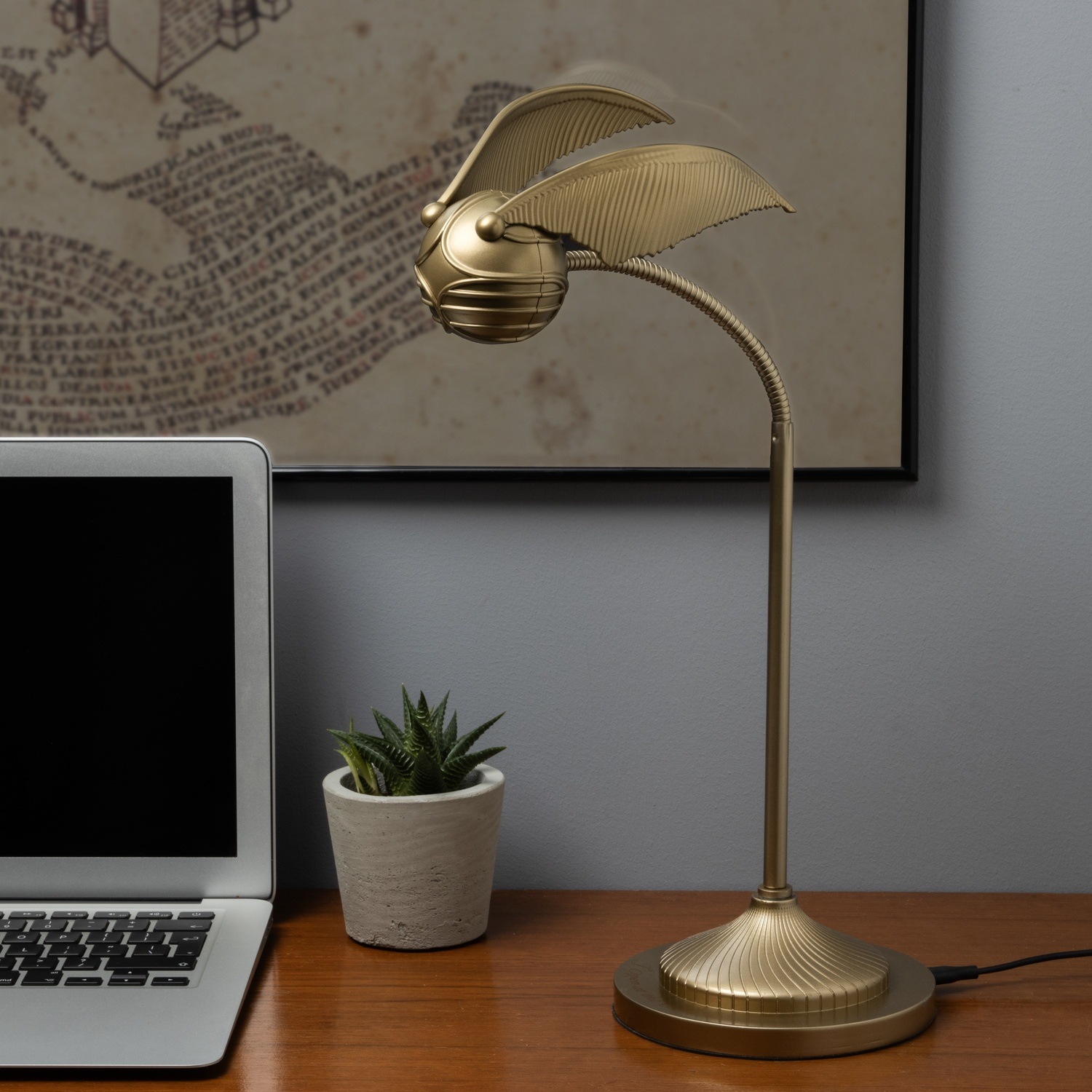 Een gouden Snitch-lamp op een bureau, met een laptop en een kleine plant.