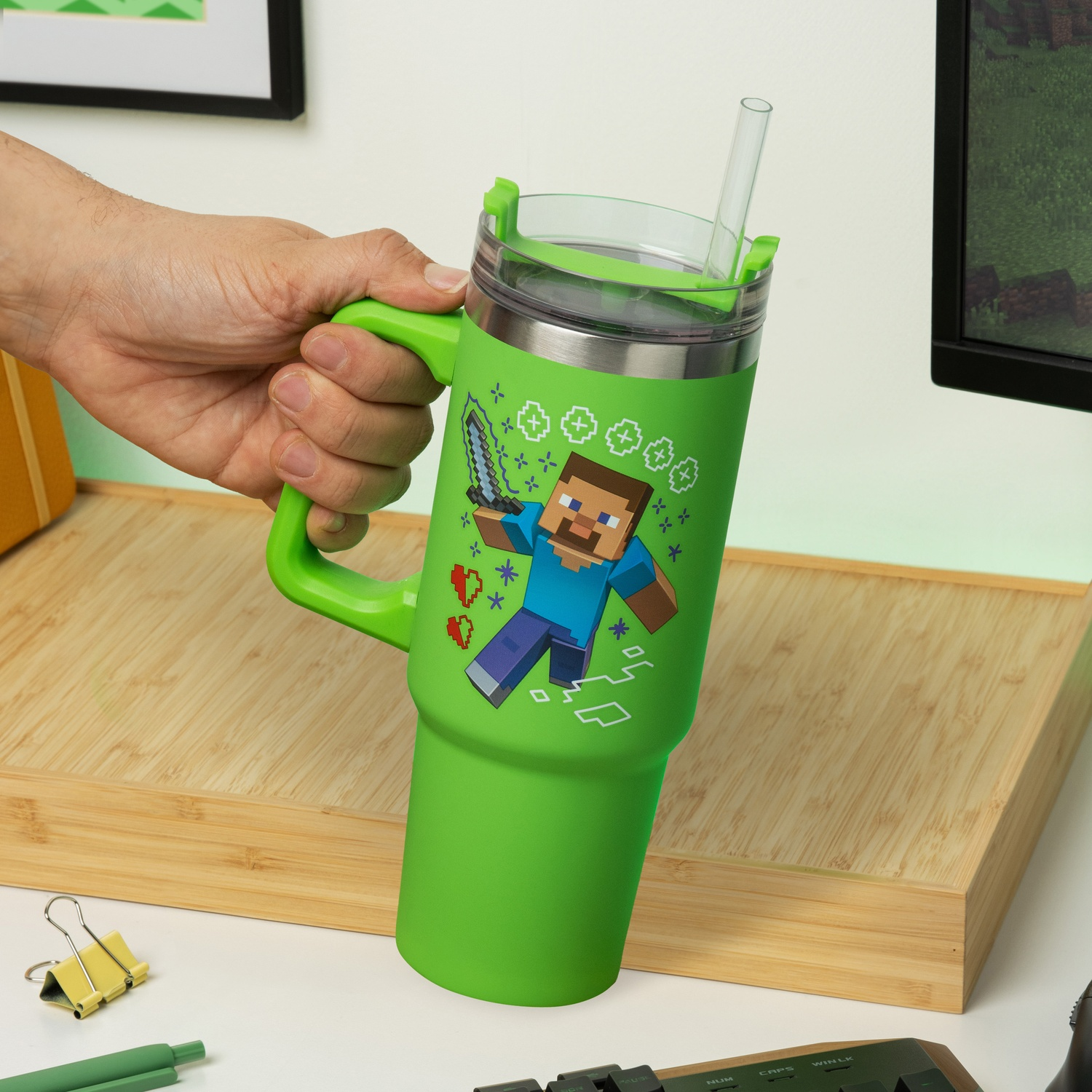 A green Minecraft themed tumbler with a straw, held by a hand.