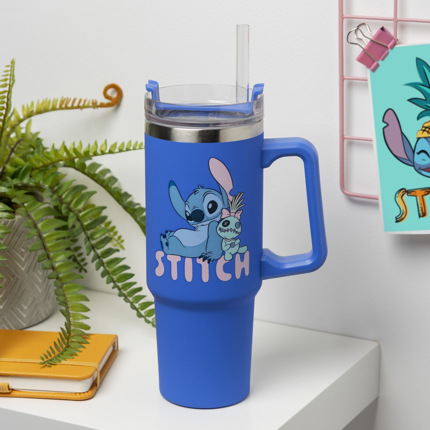 Blue Stitch tumbler with straw. Stitch graphic. On a white shelf with a plant and a notebook.