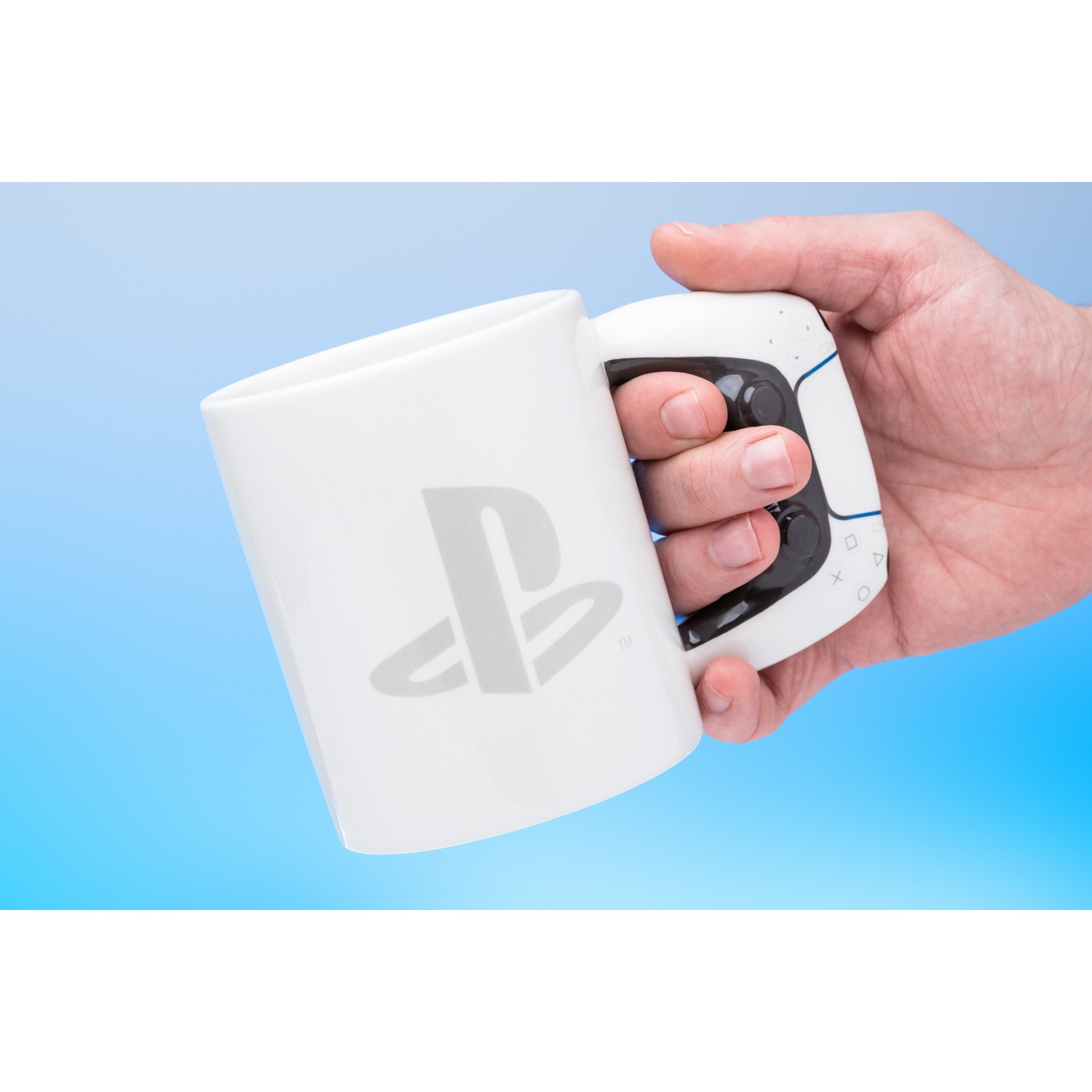A white mug with the PlayStation logo, held by a hand against a blue backdrop.