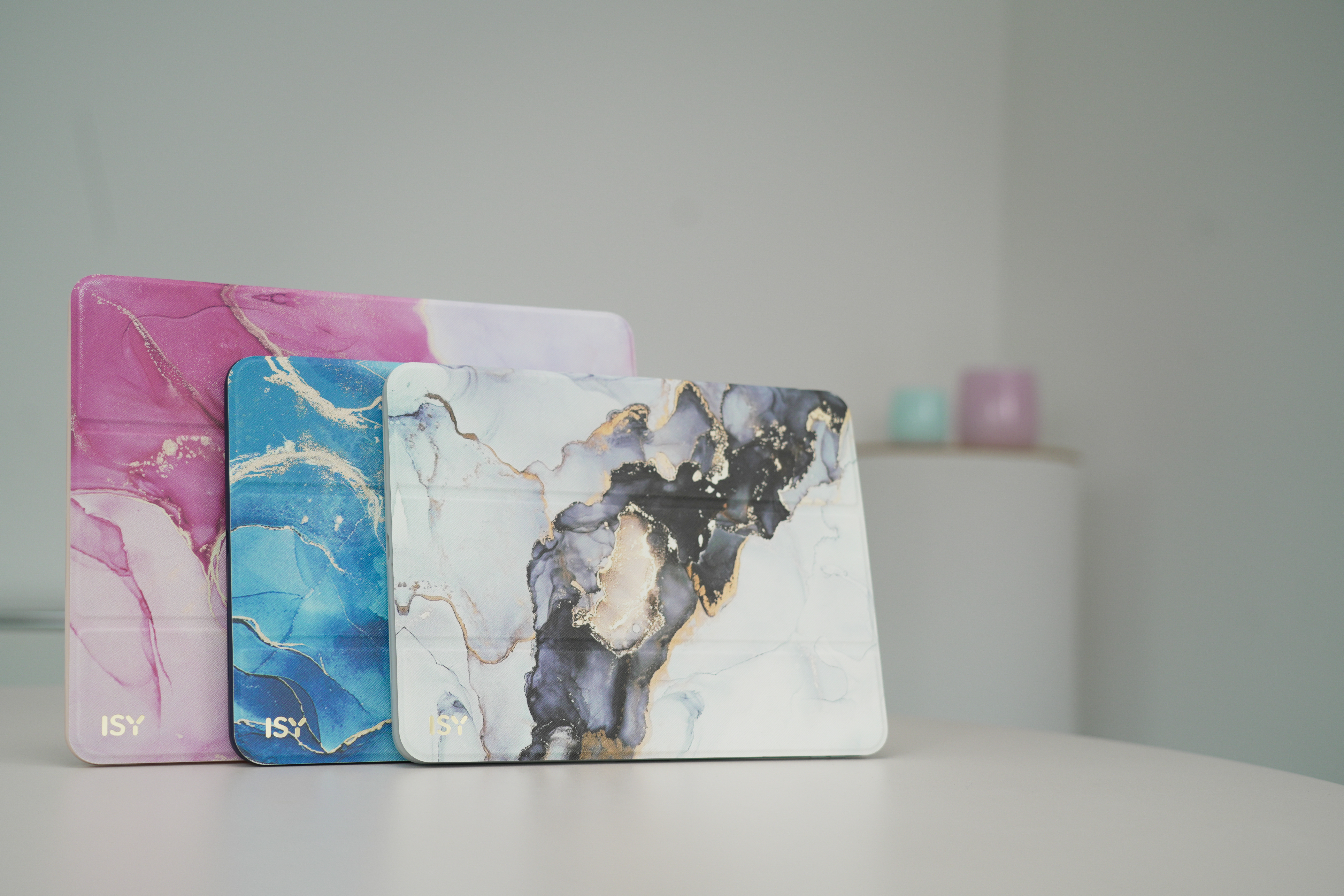 Drei dekorative Tablet-Hüllen mit marmorähnlichen Designs auf einem weißen Tisch. Der Hintergrund ist unscharf.