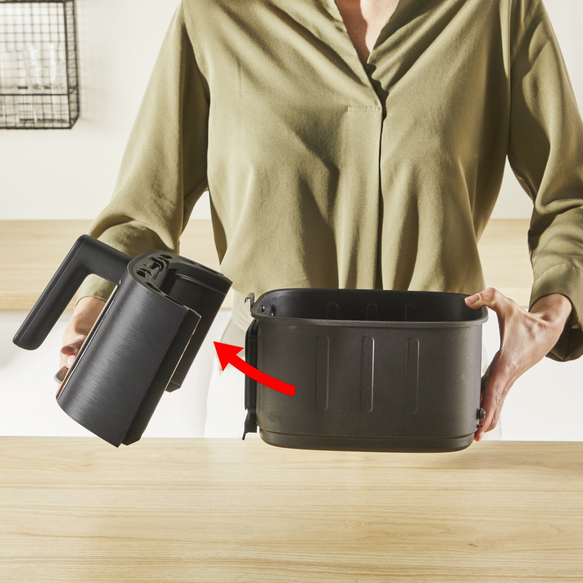 Osoba trzyma czarny pojemnik i obudowę frytkownicy. Czerwona strzałka wskazuje.
