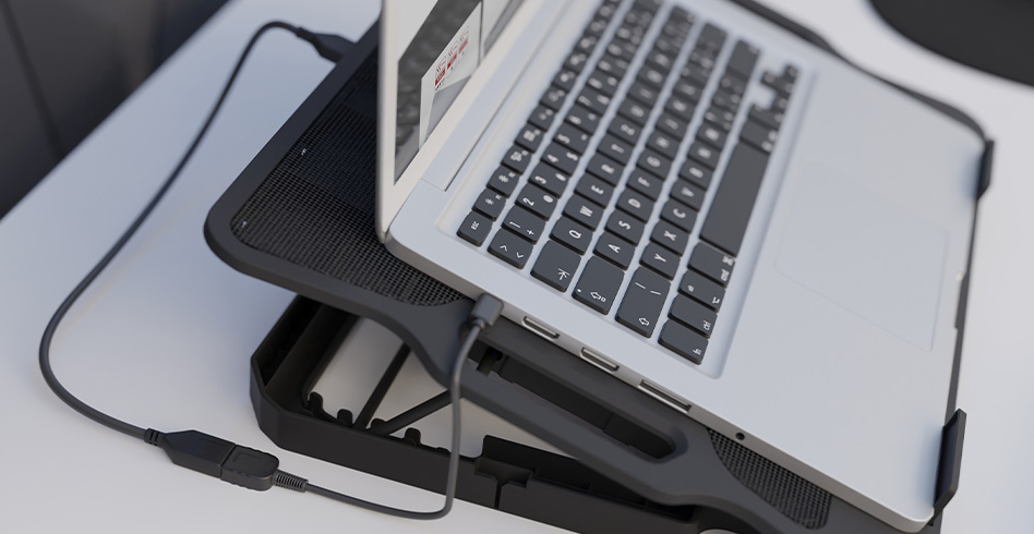 Laptop na czarnej podkładce chłodzącej. Kabel USB jest podłączony. Biała powierzchnia.