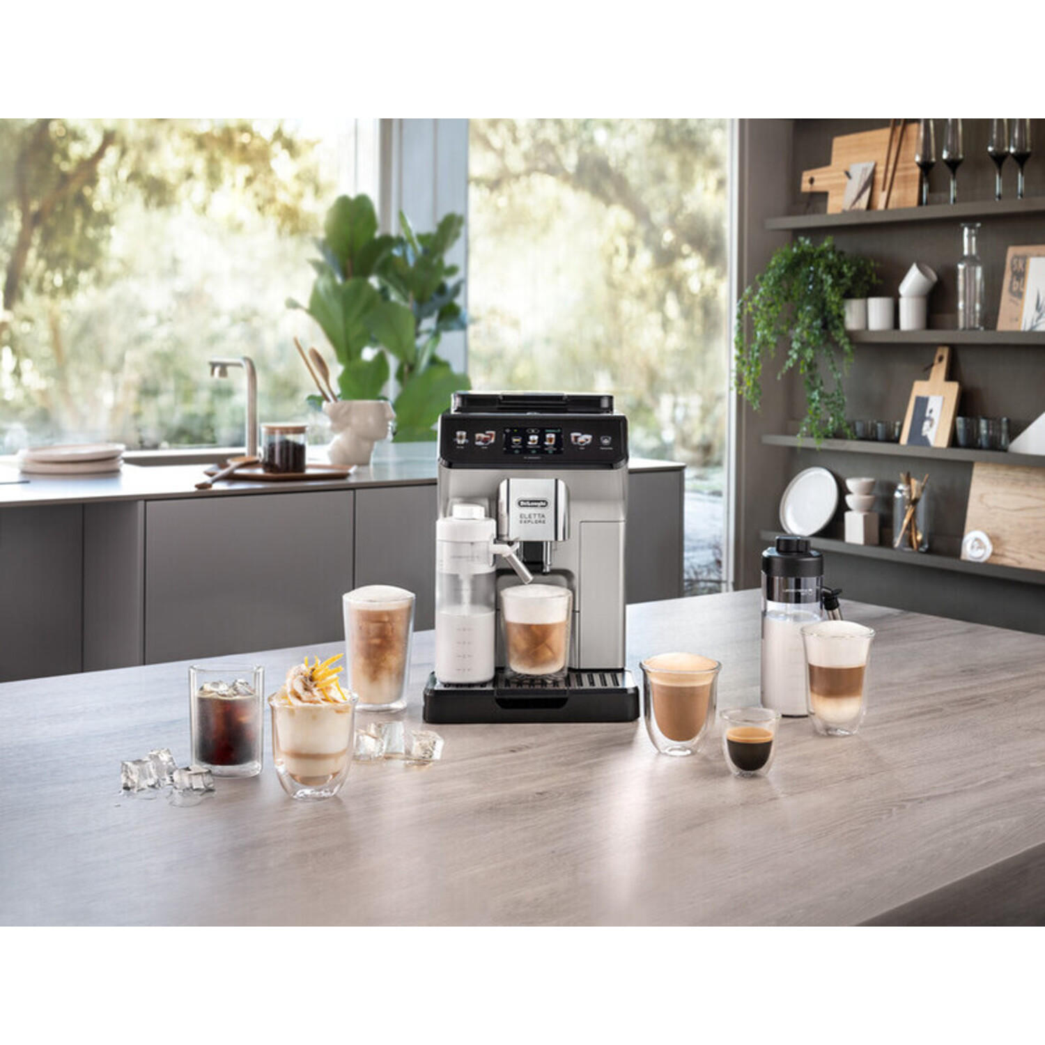 Coffee machine with various drinks and glasses on a wooden table in a bright kitchen.