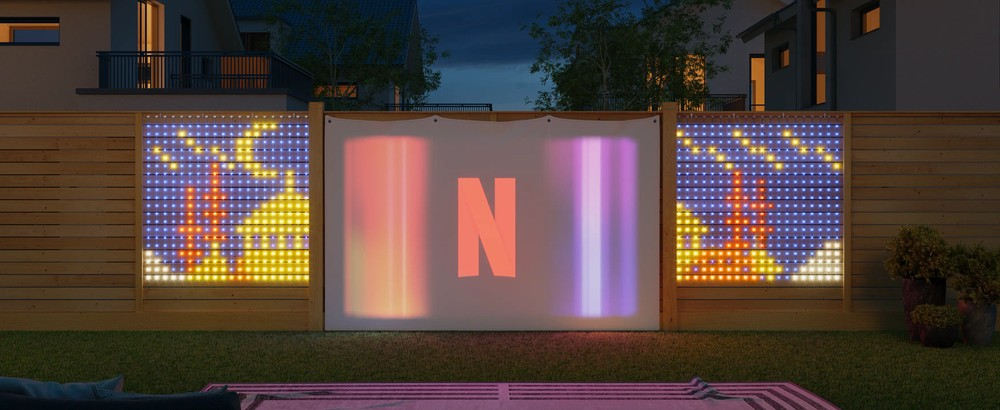 Ekran kinowy na zewnątrz z logo Netflix, otoczony światłami LED, w nocy w ogrodzie.