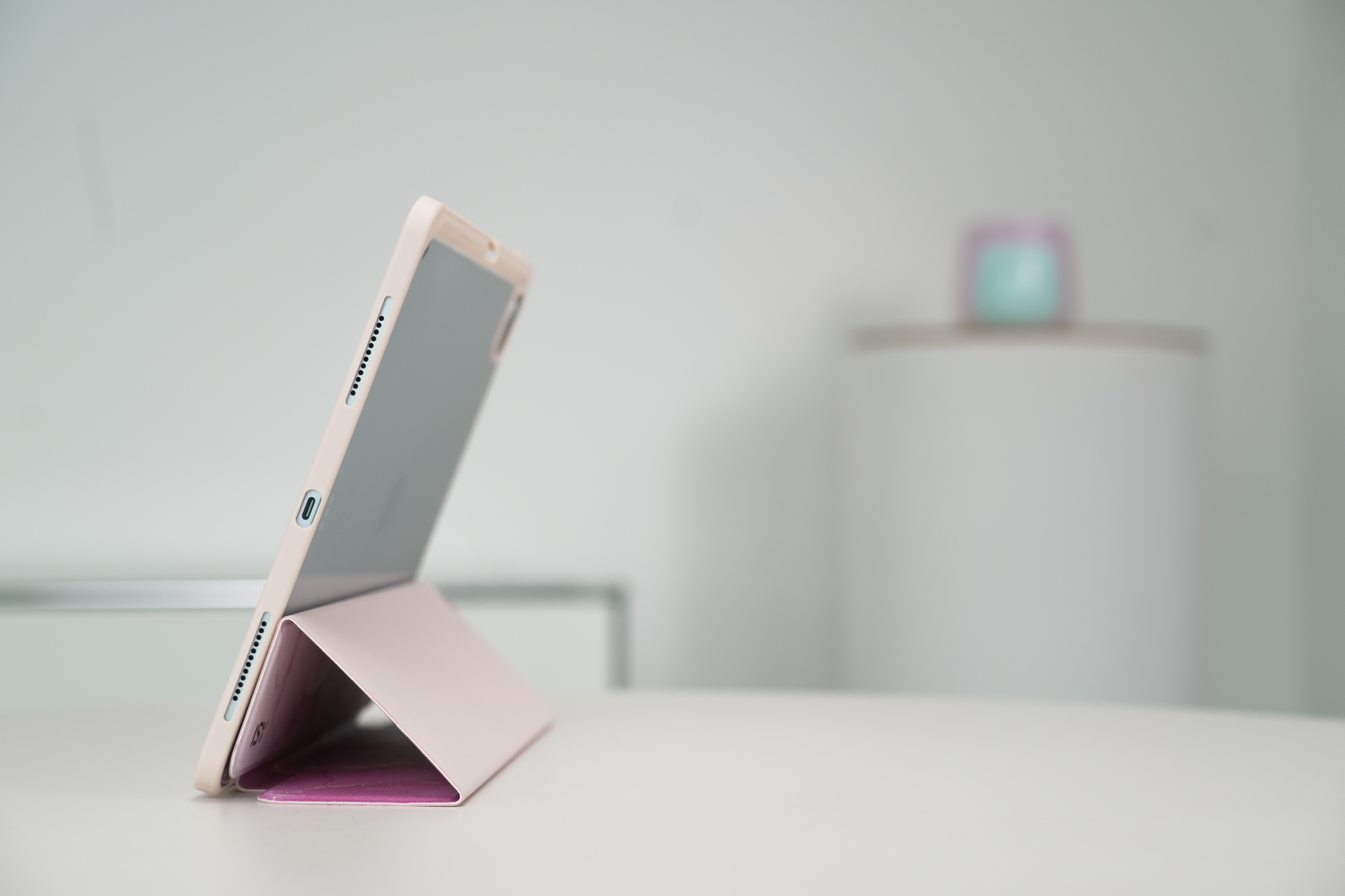 Tablet in rosa Hülle, aufgestellt. Weißer Tisch und Wand im Hintergrund.