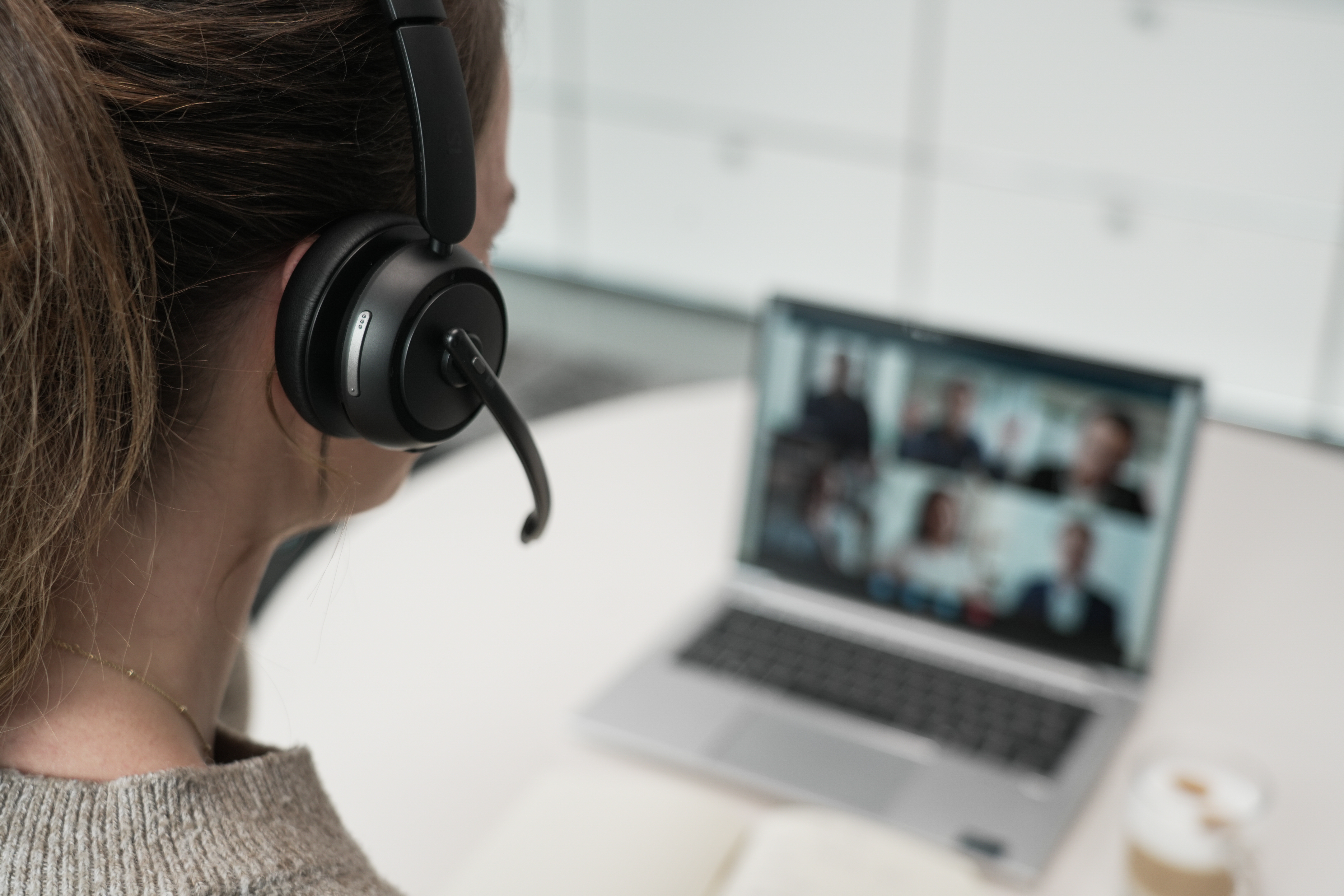 Frau mit Headset schaut auf Laptop mit Videoanruf.