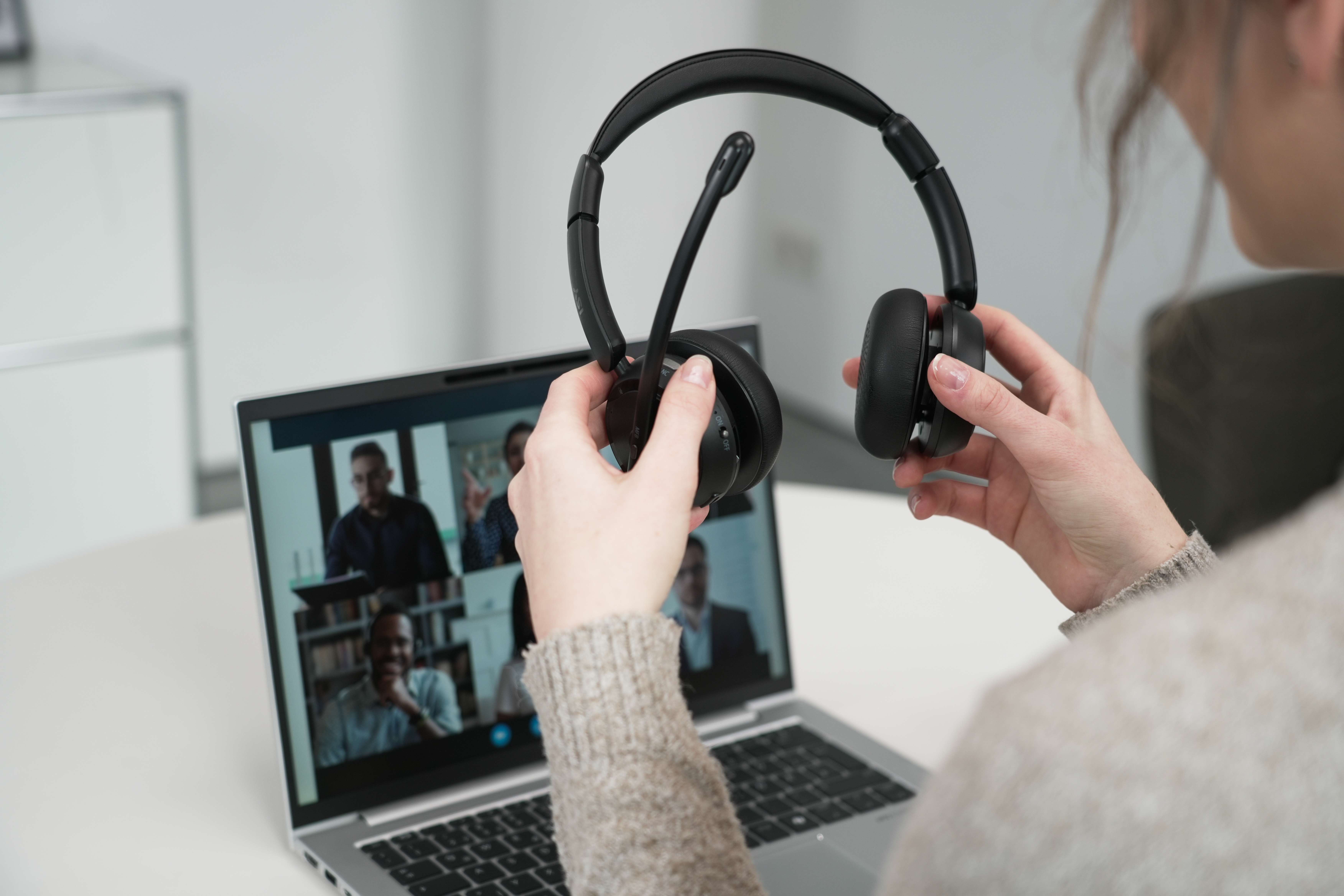 Eine Person hält ein schwarzes Headset mit Mikrofon und schaut auf einen Laptop-Bildschirm.