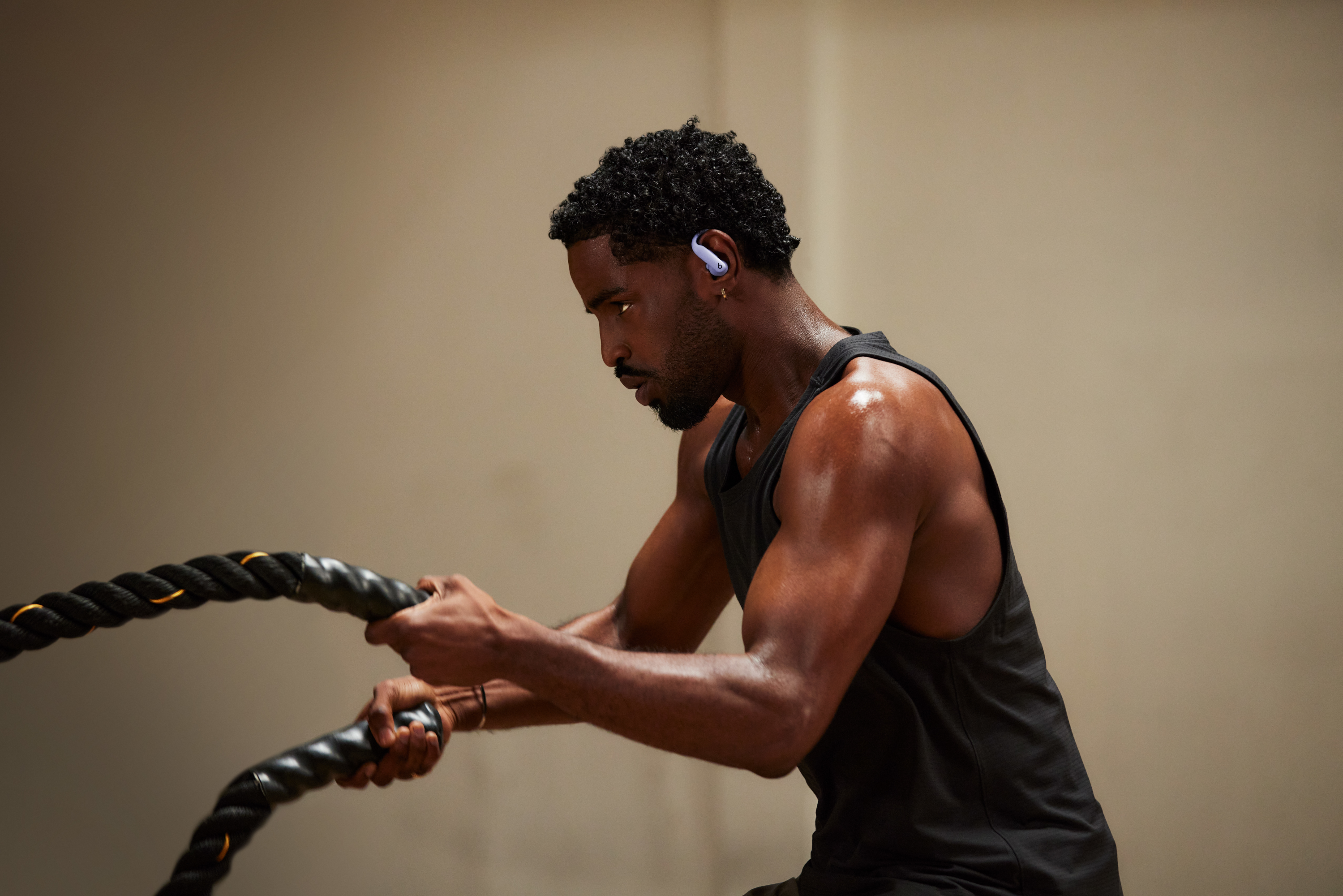 Homme en salle de sport s'entraînant avec des cordes, portant des écouteurs. Fond sombre de la salle.