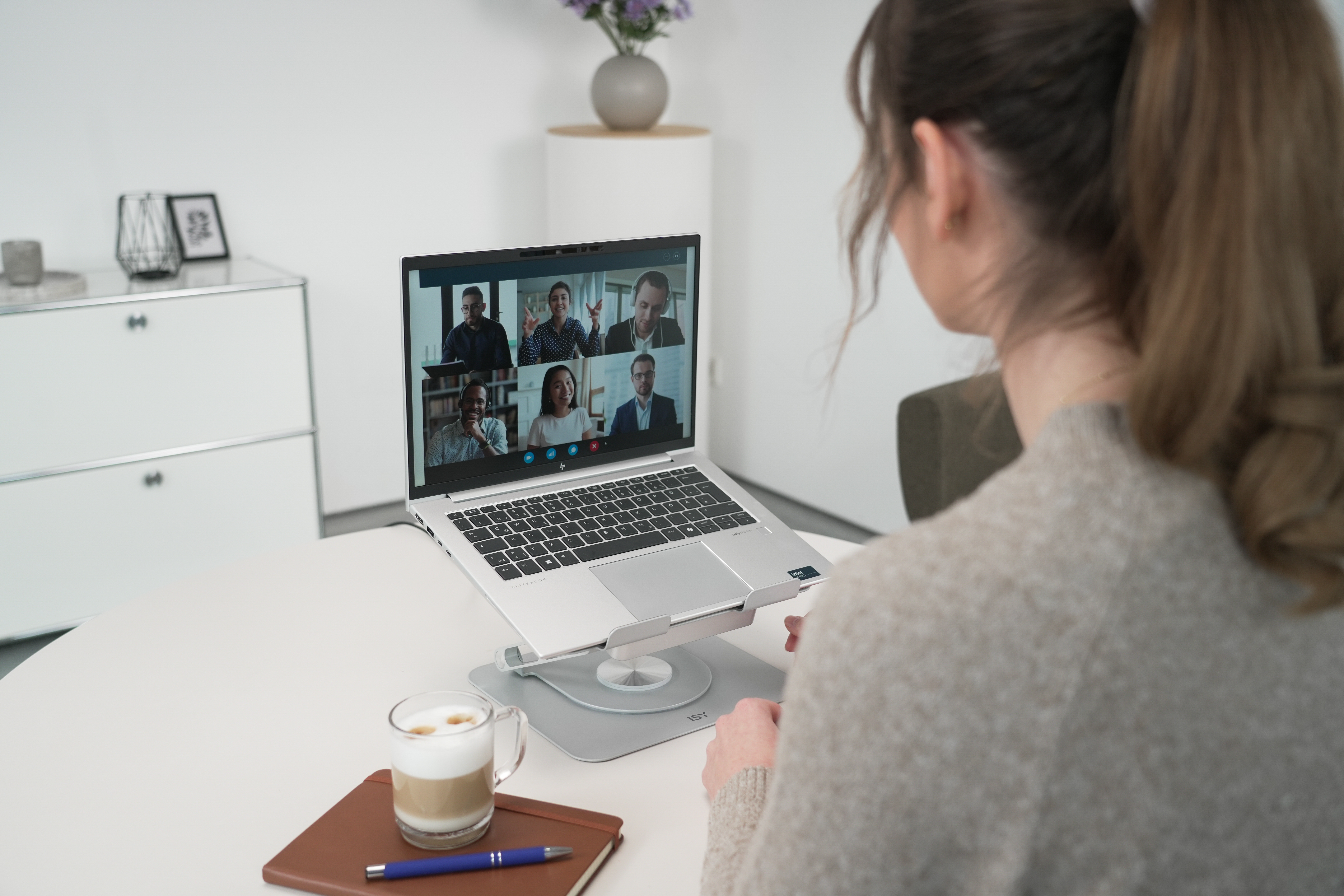 Frau in Videokonferenz auf Laptop auf Schreibtisch mit Kaffee und Notizblock.