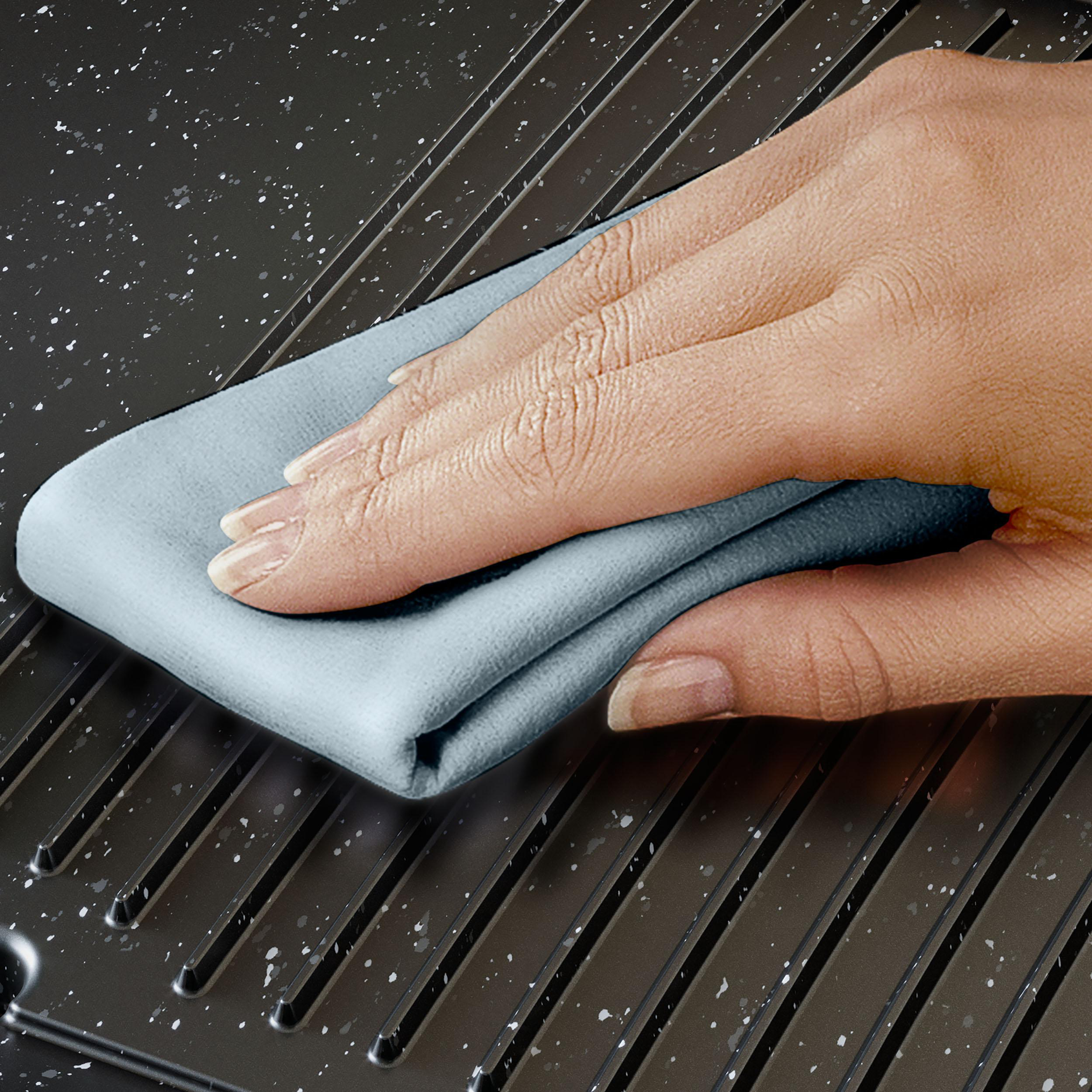 Hand reinigt Grillfläche mit blauem Tuch, weiße Punkte auf der Oberfläche.