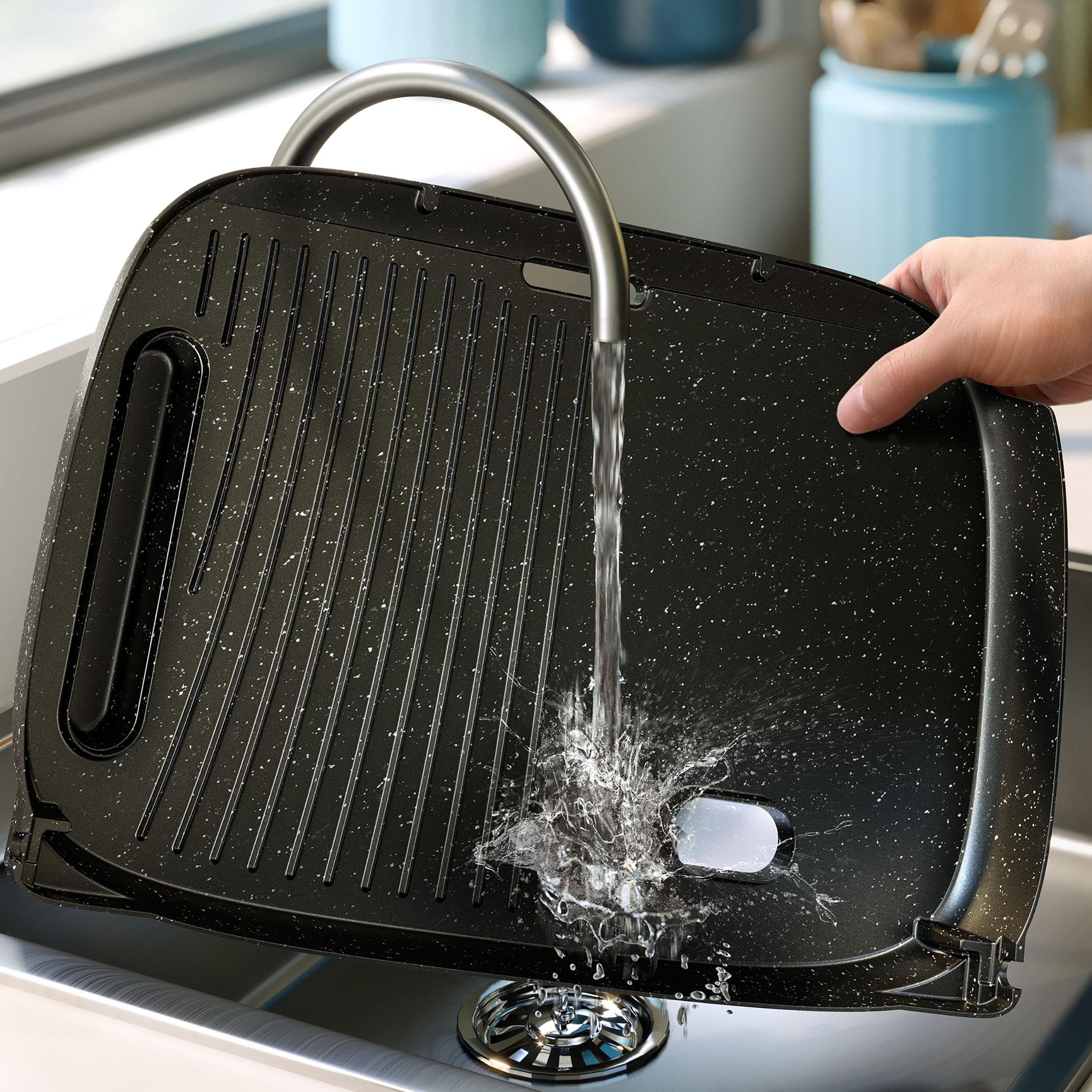 Grillpfanne unter einem Wasserhahn, wird gewaschen. Wasser spritzt aus dem Wasserhahn.