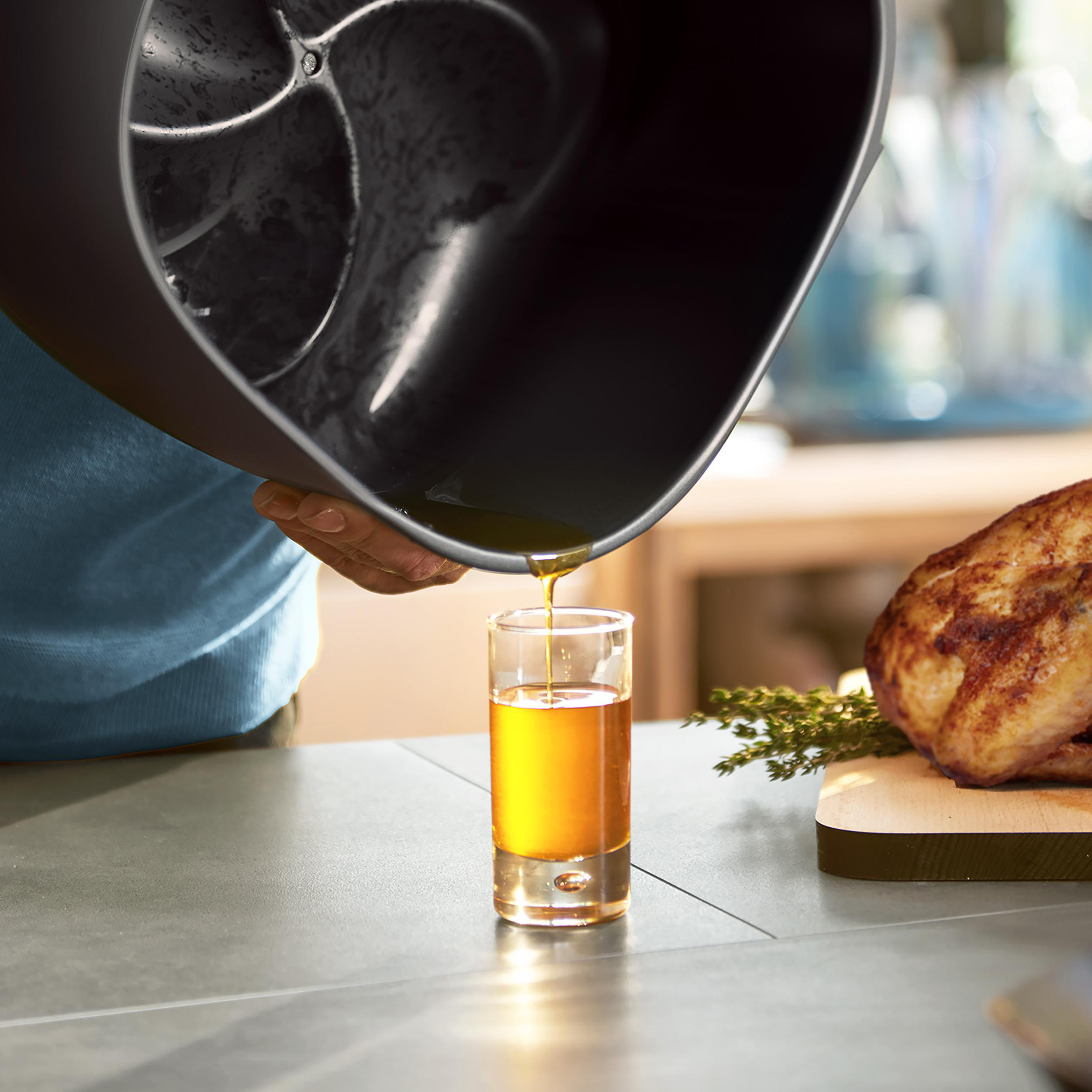 Eine Person gießt Öl in ein Schnapsglas neben einem Huhn und Rosmarin.