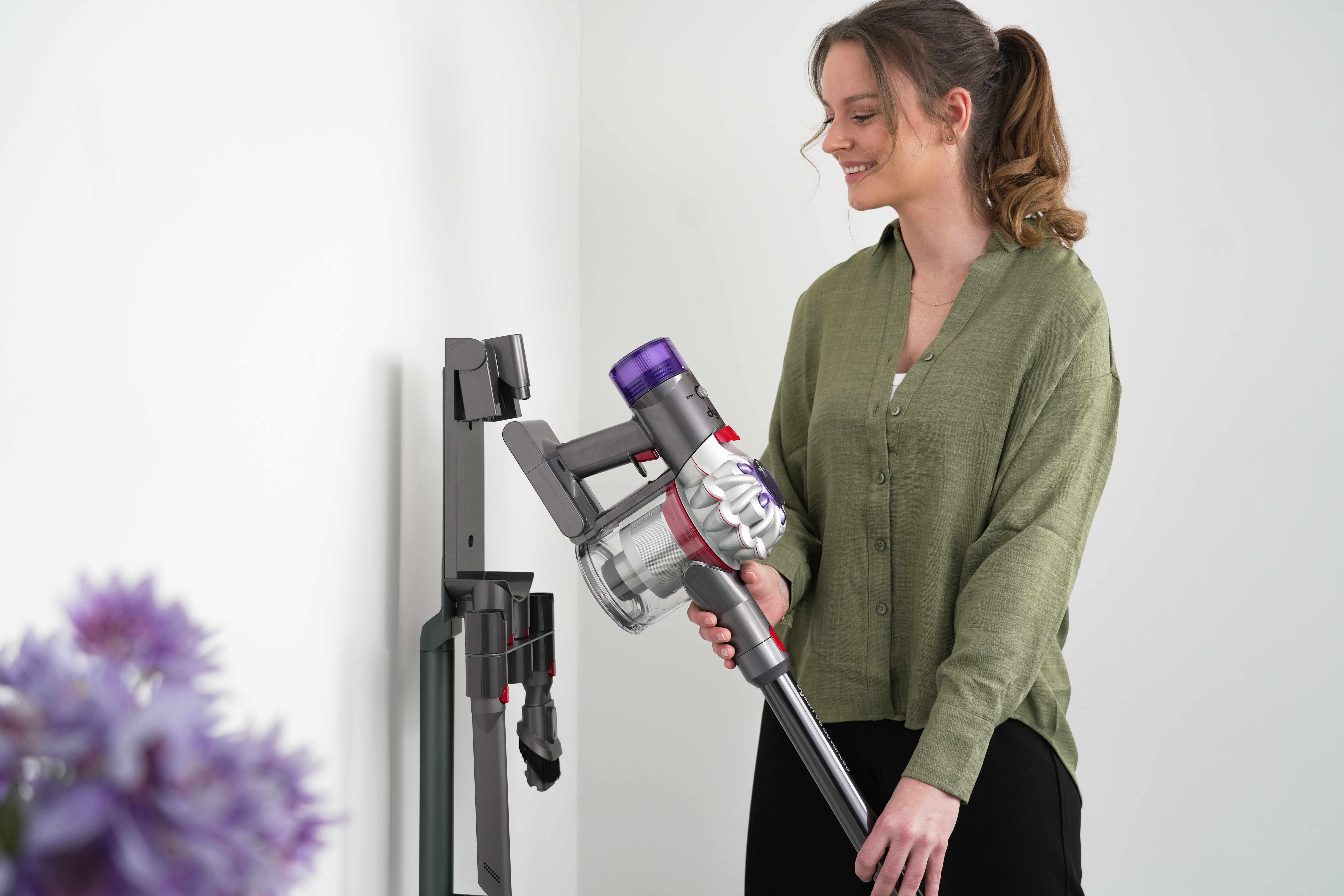 Frau benutzt Dyson-Staubsauger, lehnt an weißer Wand.