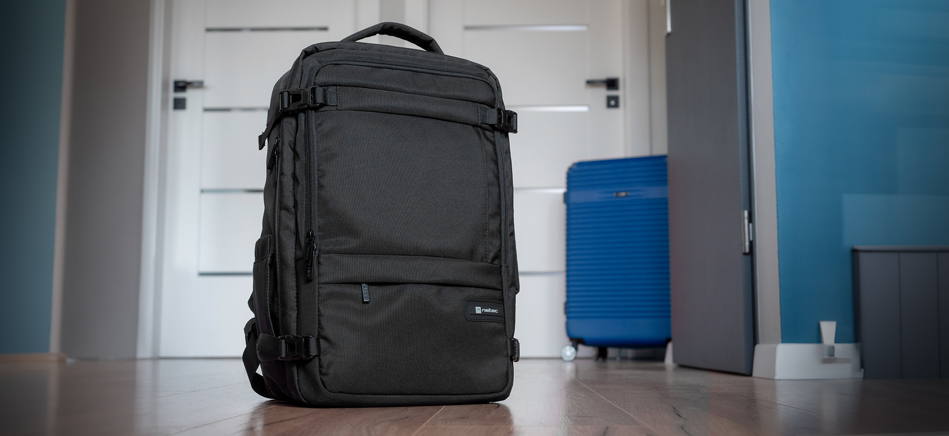 Czarny plecak i niebieska walizka w korytarzu mieszkania.