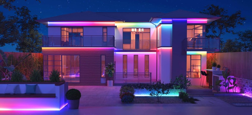 Dom z kolorowymi światłami LED. Jest noc. Drzewa i krzewy na pierwszym planie.