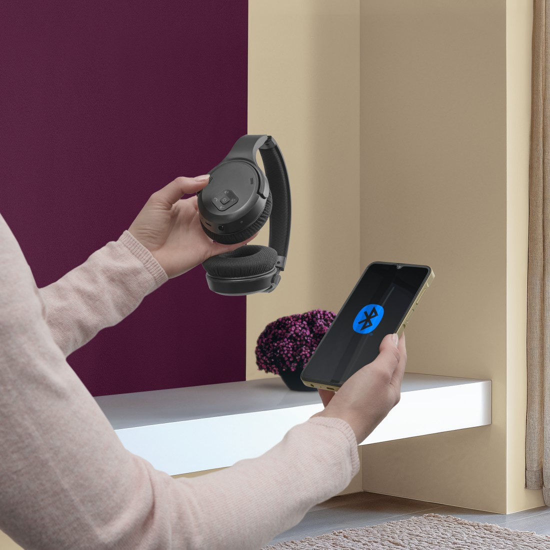 Une personne tient un casque noir et un smartphone avec une icône Bluetooth.