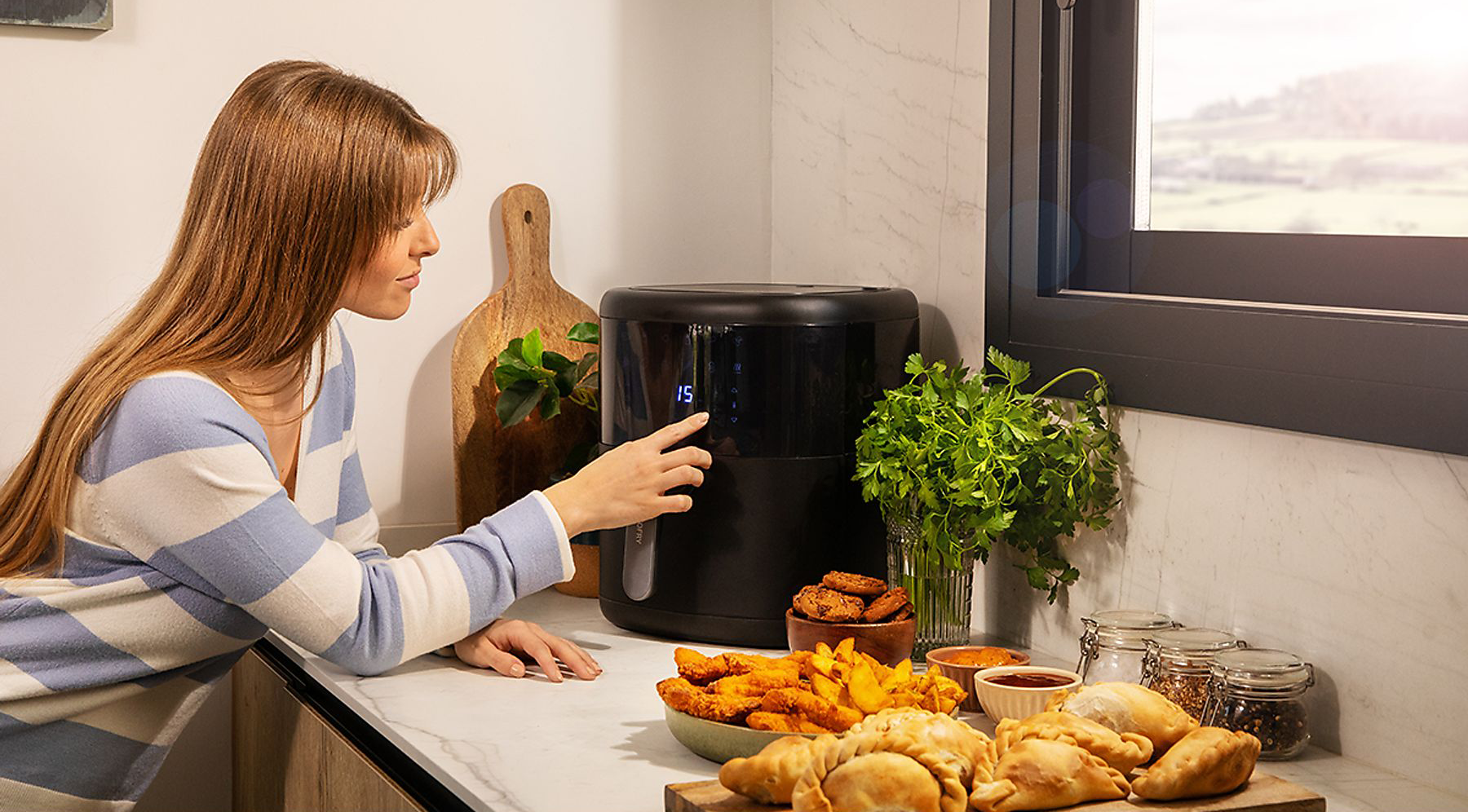 Egy nő megérinti a digitális légsütő vezérlőpanelt; ételek a pulton.