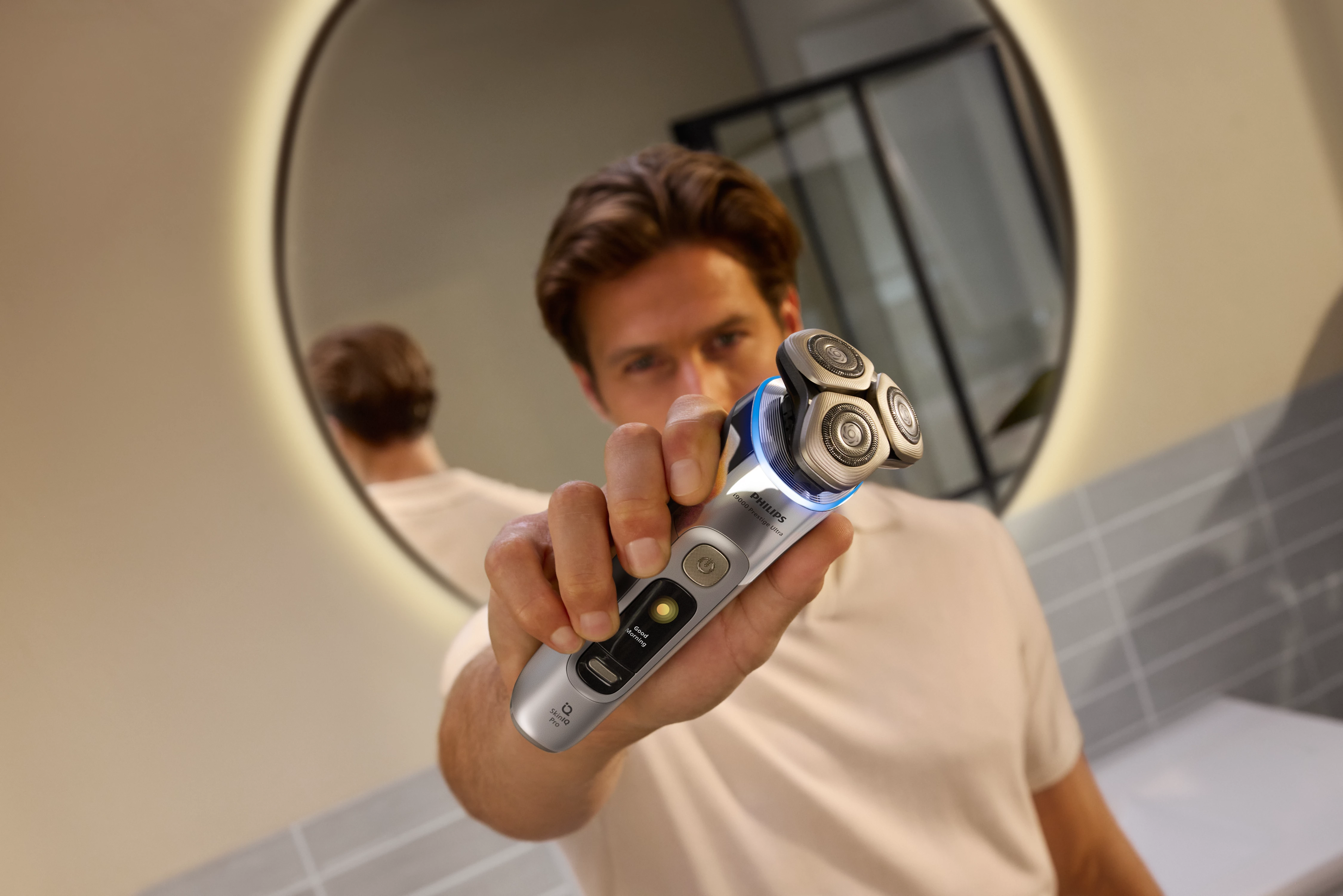 Mann hält einen silbernen Elektrorasierer und blickt in einen Spiegel. Badezimmer-Einstellung.