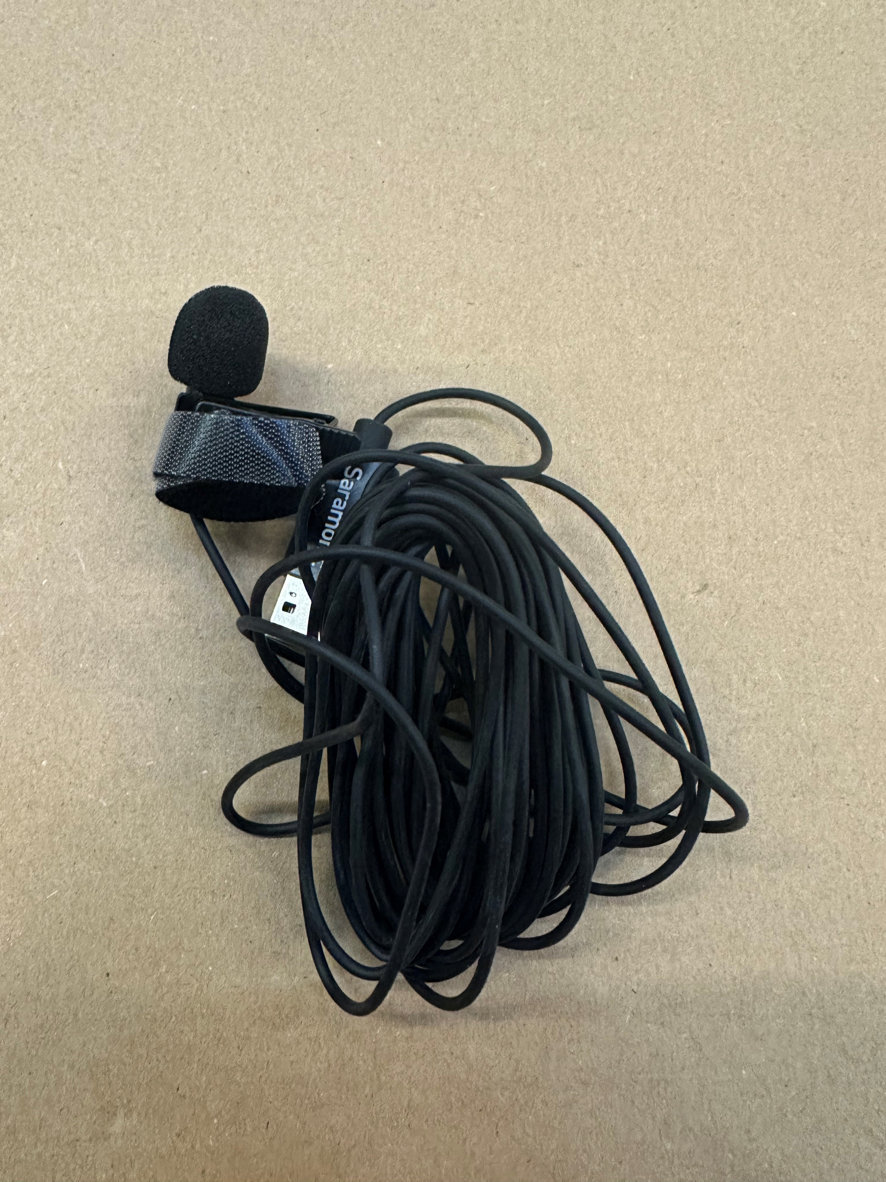 Czarny mikrofon z czarną piankową osłoną i czarnym kablem na beżowej powierzchni.