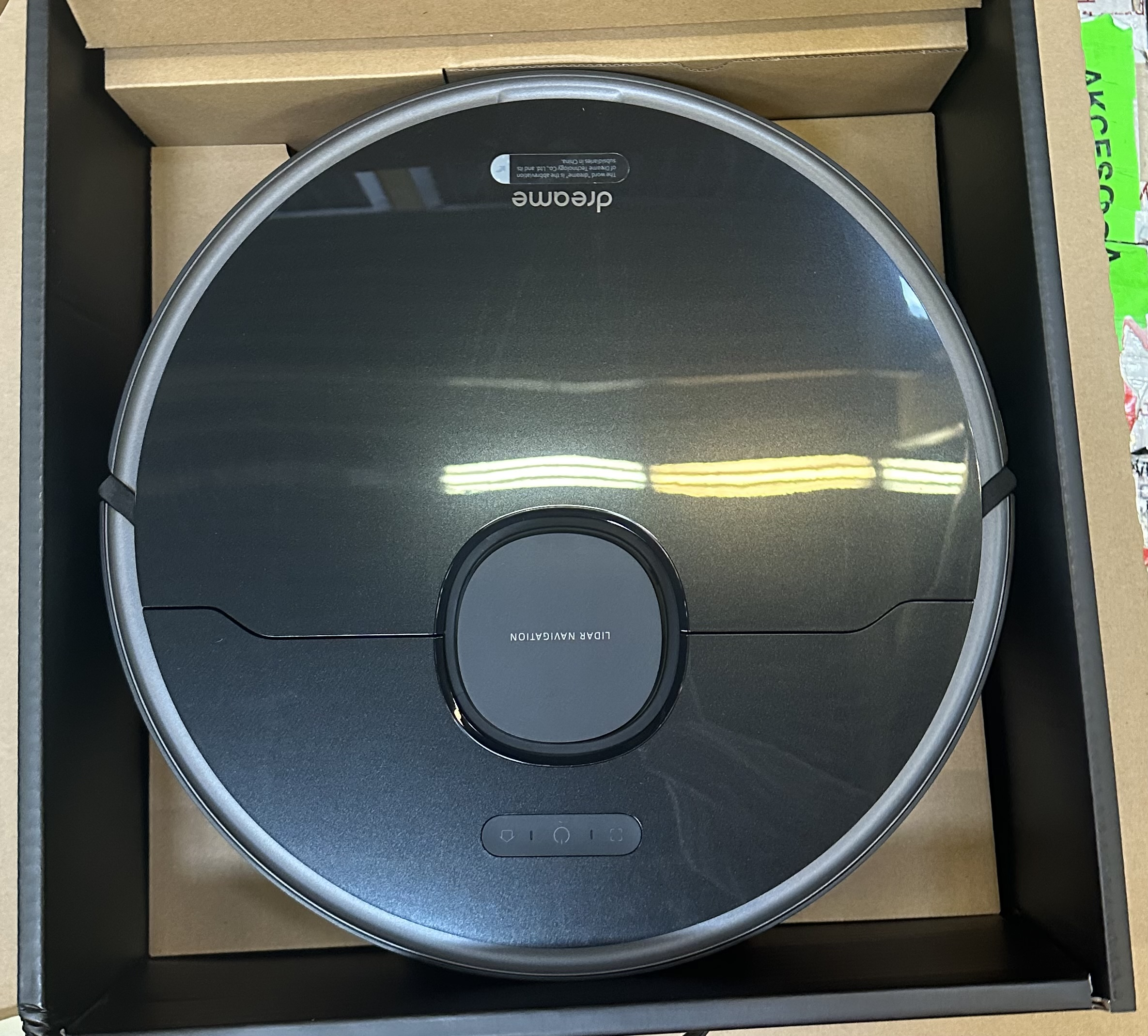 Czarny robot odkurzający Dreame w pudełku. Otwarta pokrywa, widoczny górny panel z szczegółami nawigacji.