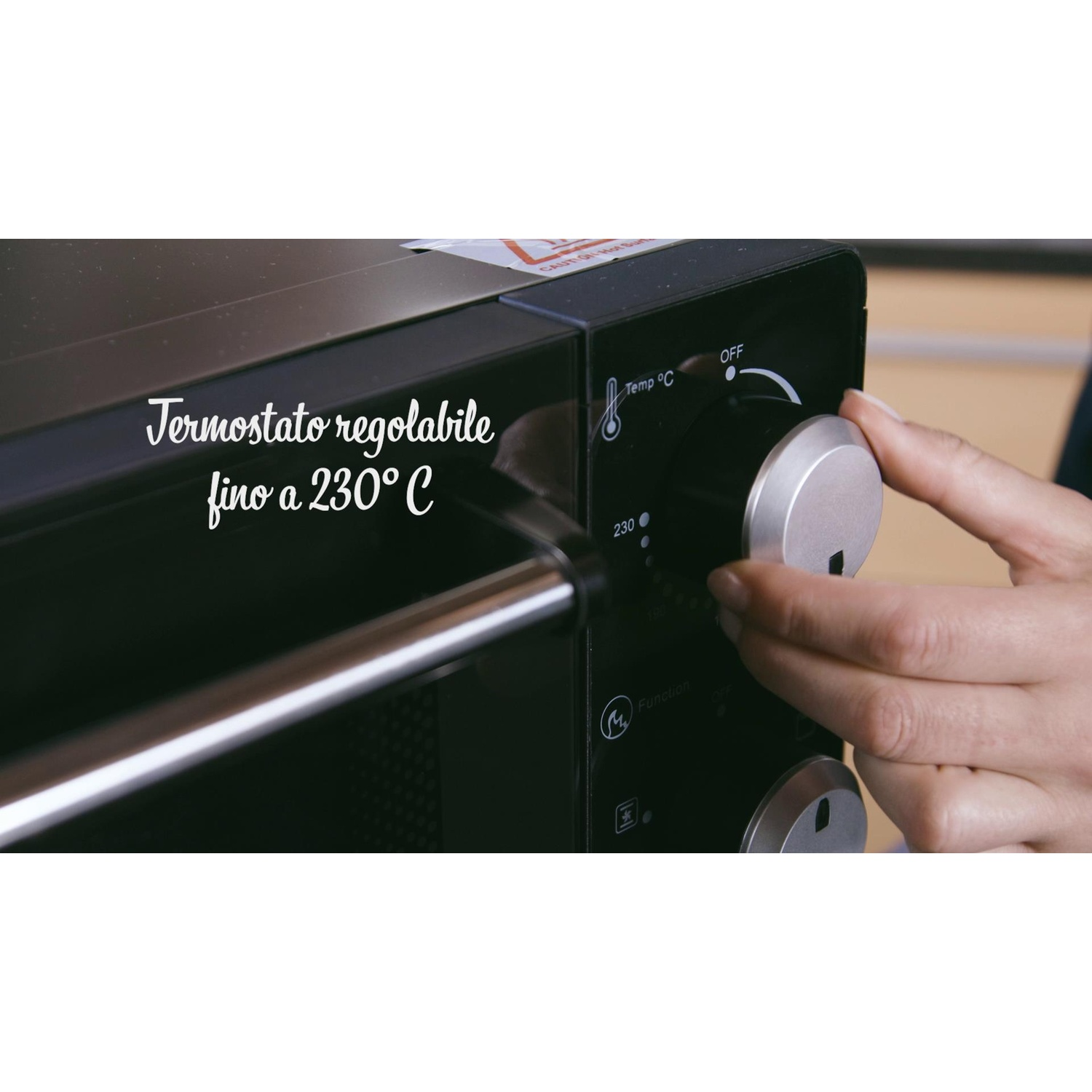 Una mano che ruota la manopola della temperatura su un forno nero.