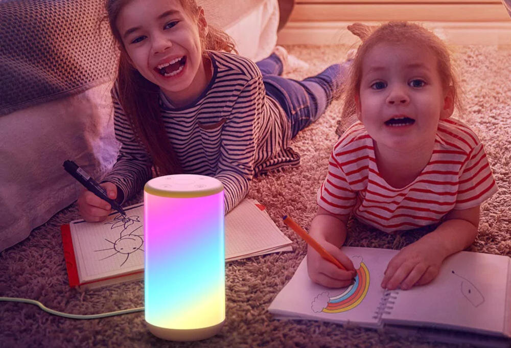 Dwoje dzieci rysuje kredkami w pobliżu lampy zmieniającej kolory na dywanie.