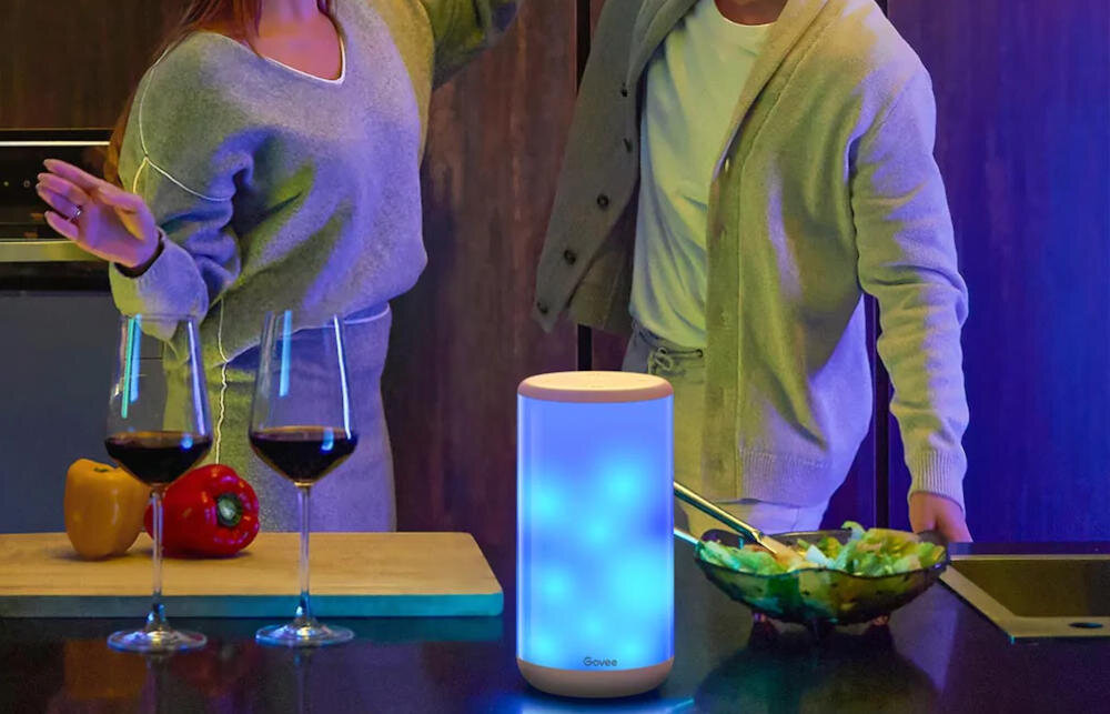 Para z kieliszkami wina w kuchni ze zmieniającą kolory lampą i miską sałaty na blacie.