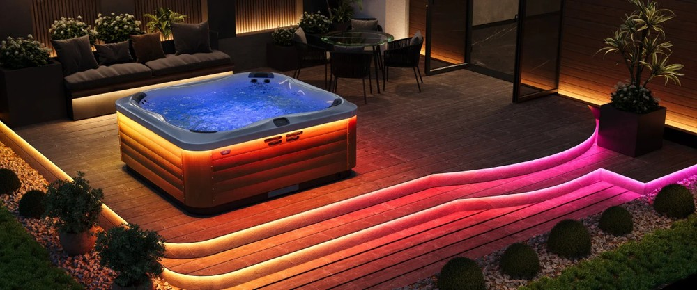 Jacuzzi ze światłami na drewnianym tarasie z roślinami w otoczeniu nocnym.