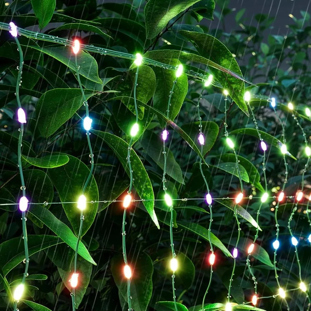 Zbliżenie wielokolorowych lampek na zielonych roślinach, z efektem deszczu.